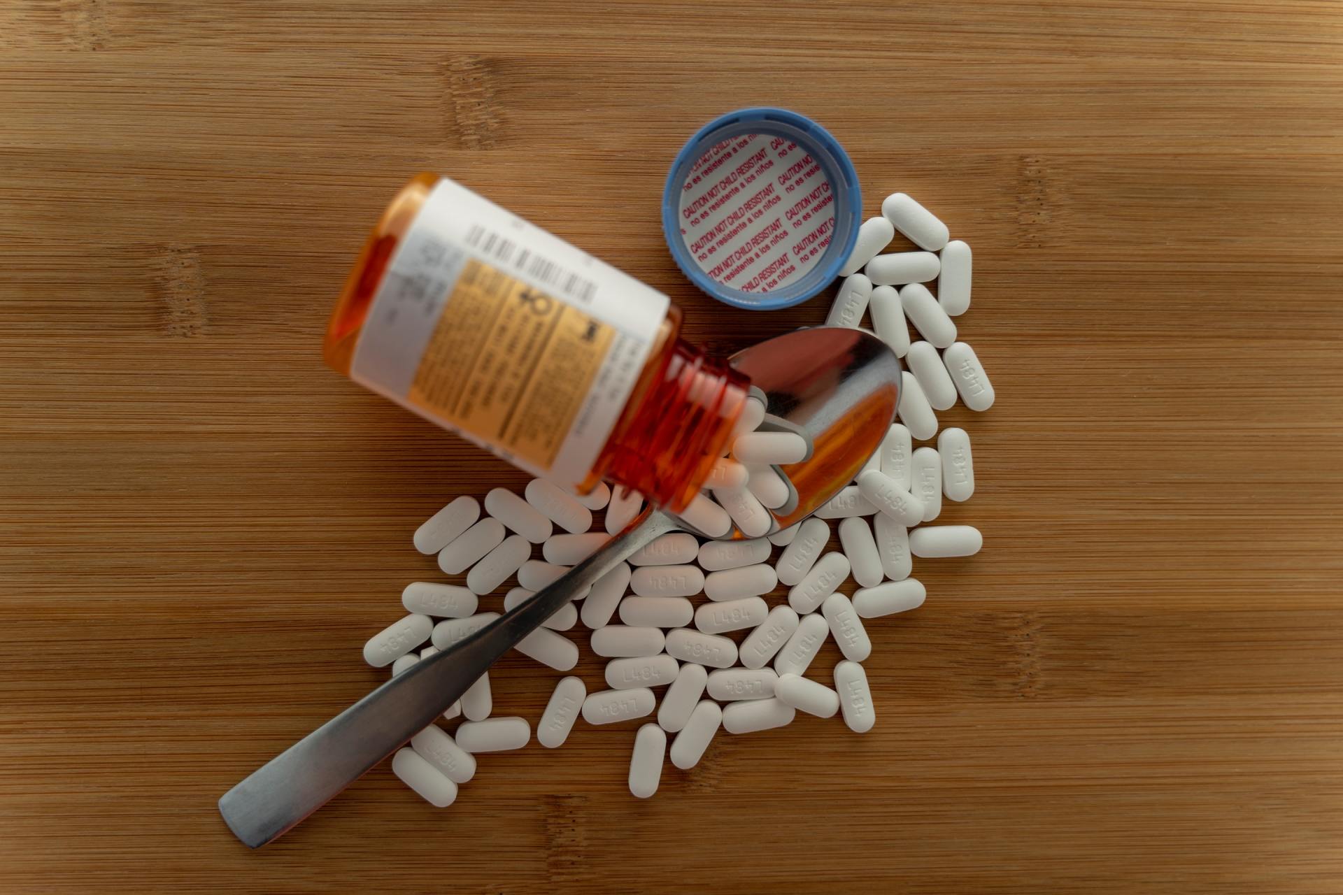 A bottle of pills is spilling out of it on a wooden table.