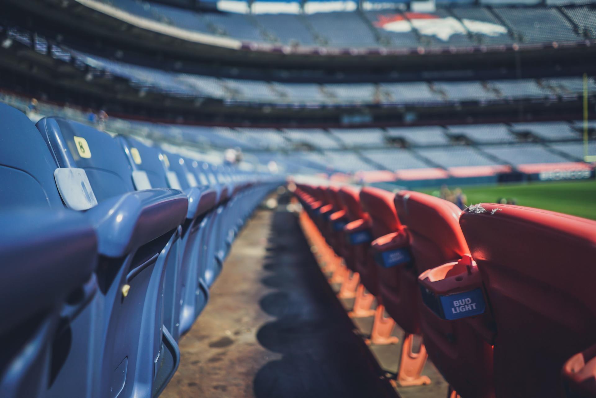 Leere blaue und rote Stadionsitze säumen einen Gang im hellen Sonnenlicht.