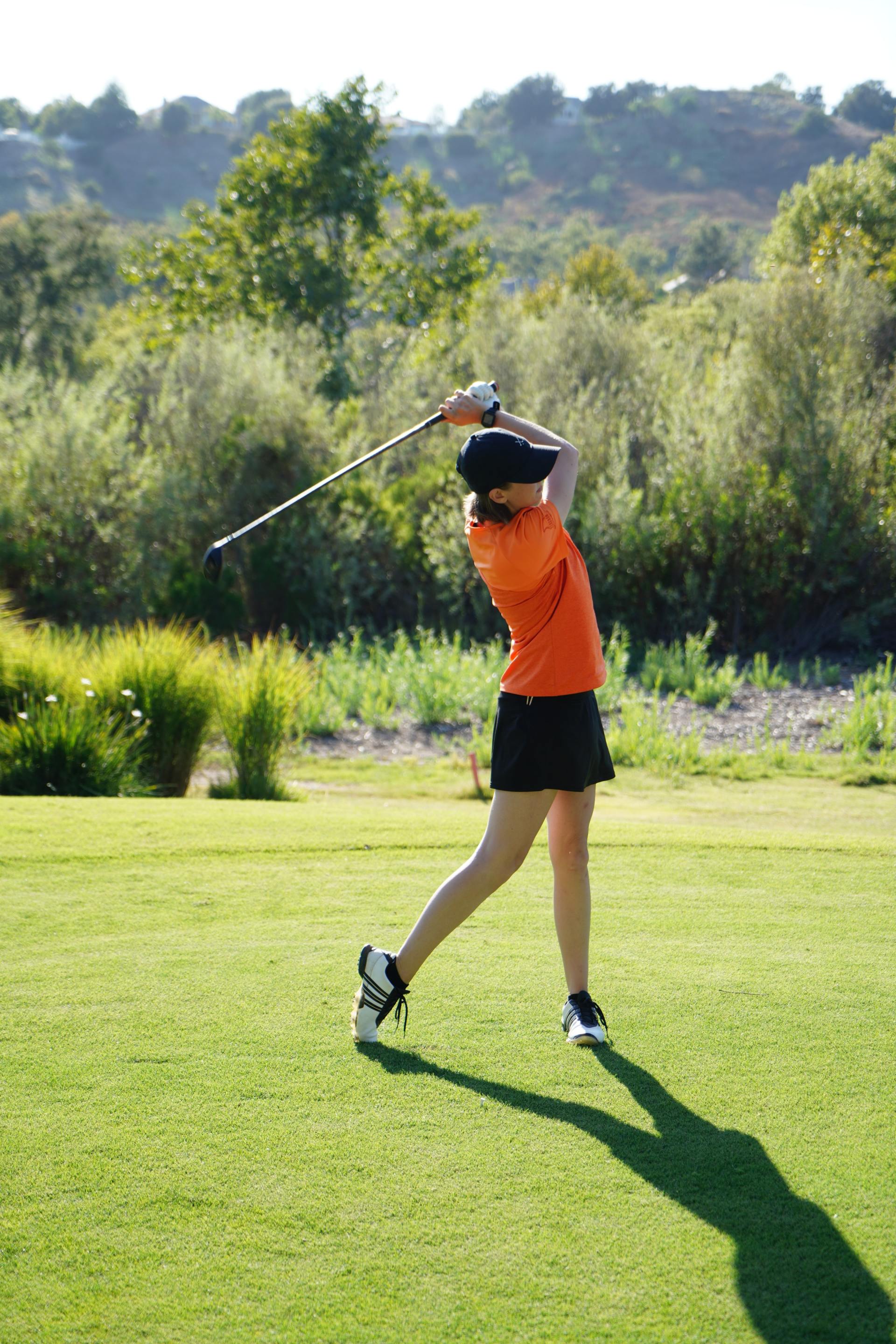 A woman is swinging a golf club on a golf course.