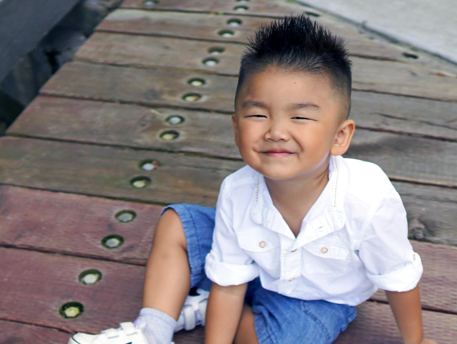 A young boy is sitting on a wooden deck and smiling