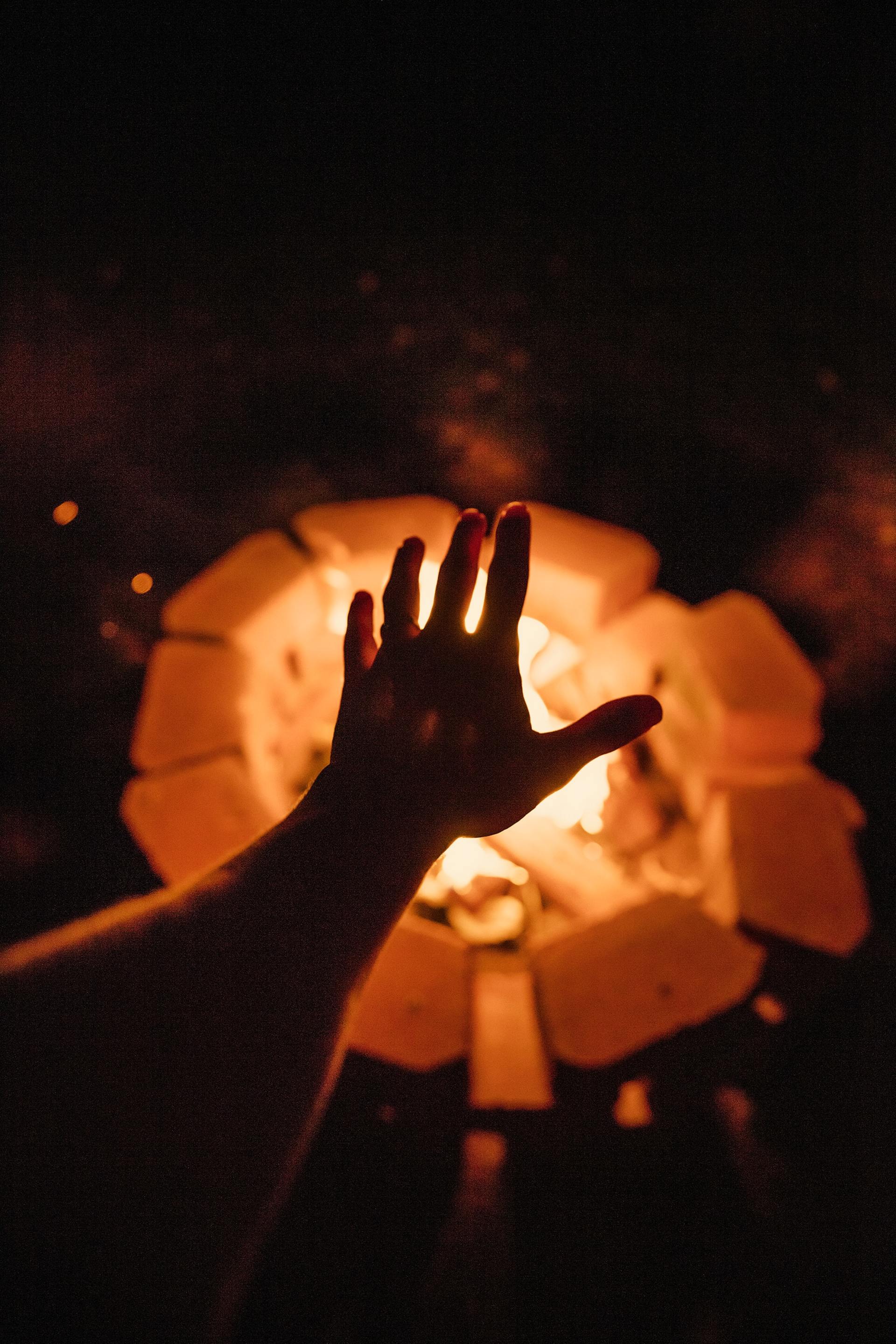 a person 's hand is reaching out towards a fire pit at night .