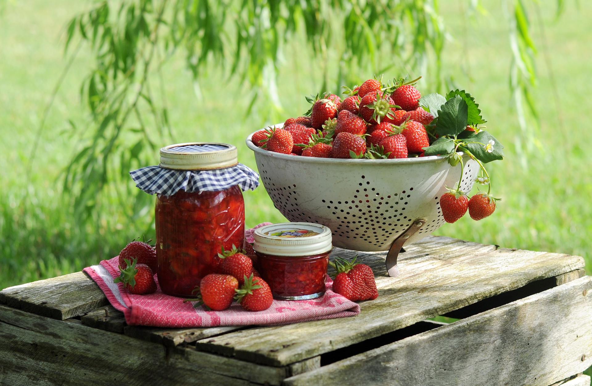Un bol de fraises et un pot de confiture sont sur une table en bois.