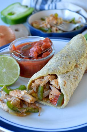 A tortilla wrap with chicken , peppers , onions and tomato sauce on a plate.