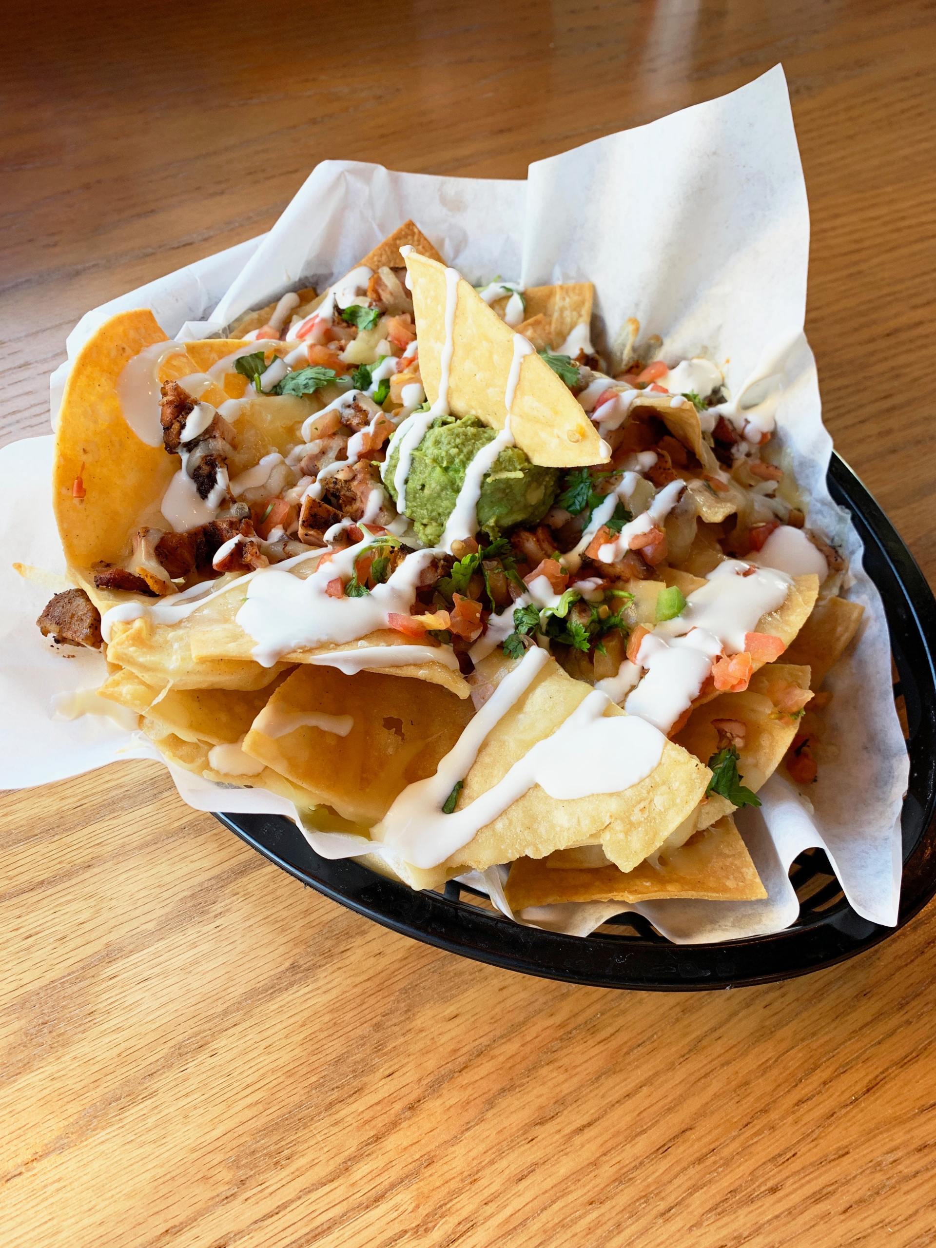 Nachos in a basket with toppings: meat, guacamole, salsa, and drizzled sauce.