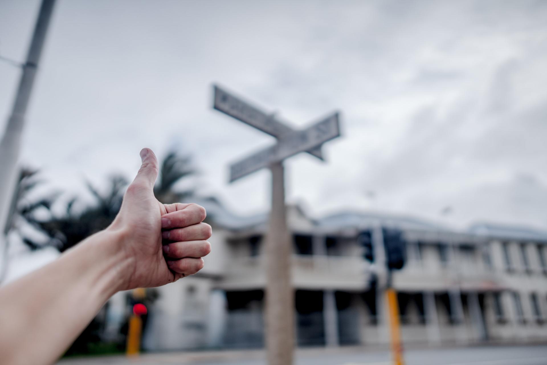 A person is giving a thumbs up in front of a street sign.
