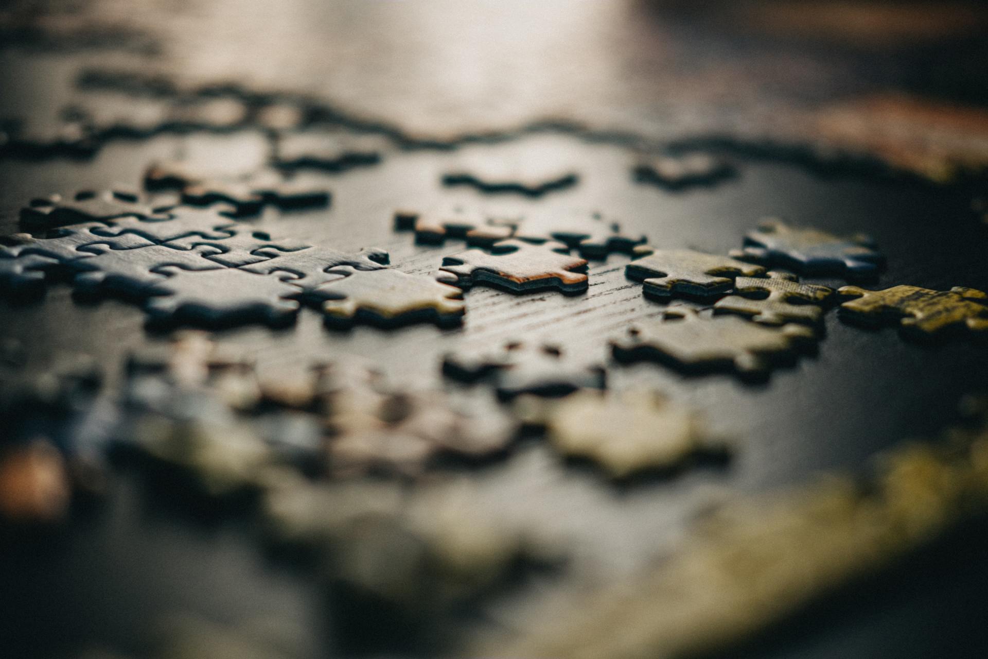 Close-up of scattered jigsaw puzzle pieces on a dark surface, with a shallow depth of field.