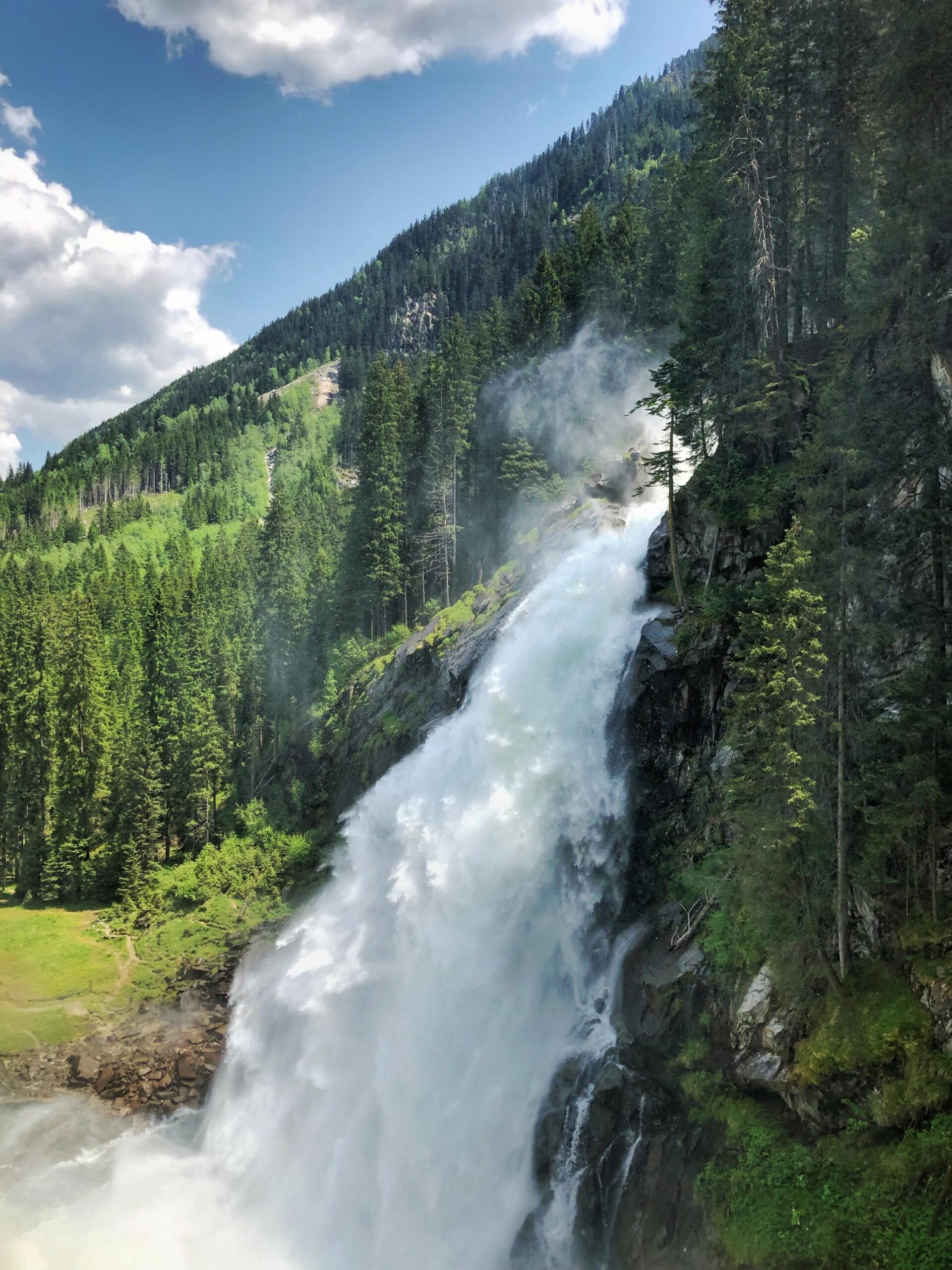 Ein hoher Wasserfall stürzt unter einem teilweise bewölkten Himmel einen bewaldeten Berg hinab.