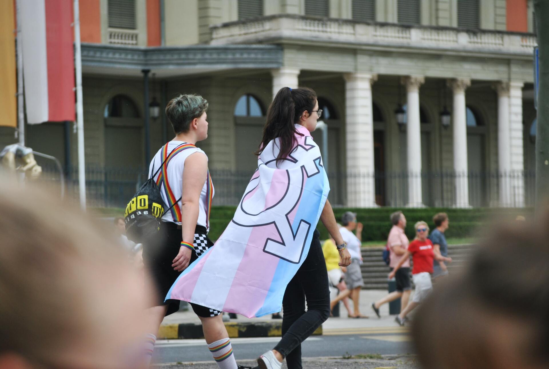 A woman is carrying a transgender flag while walking down the street.