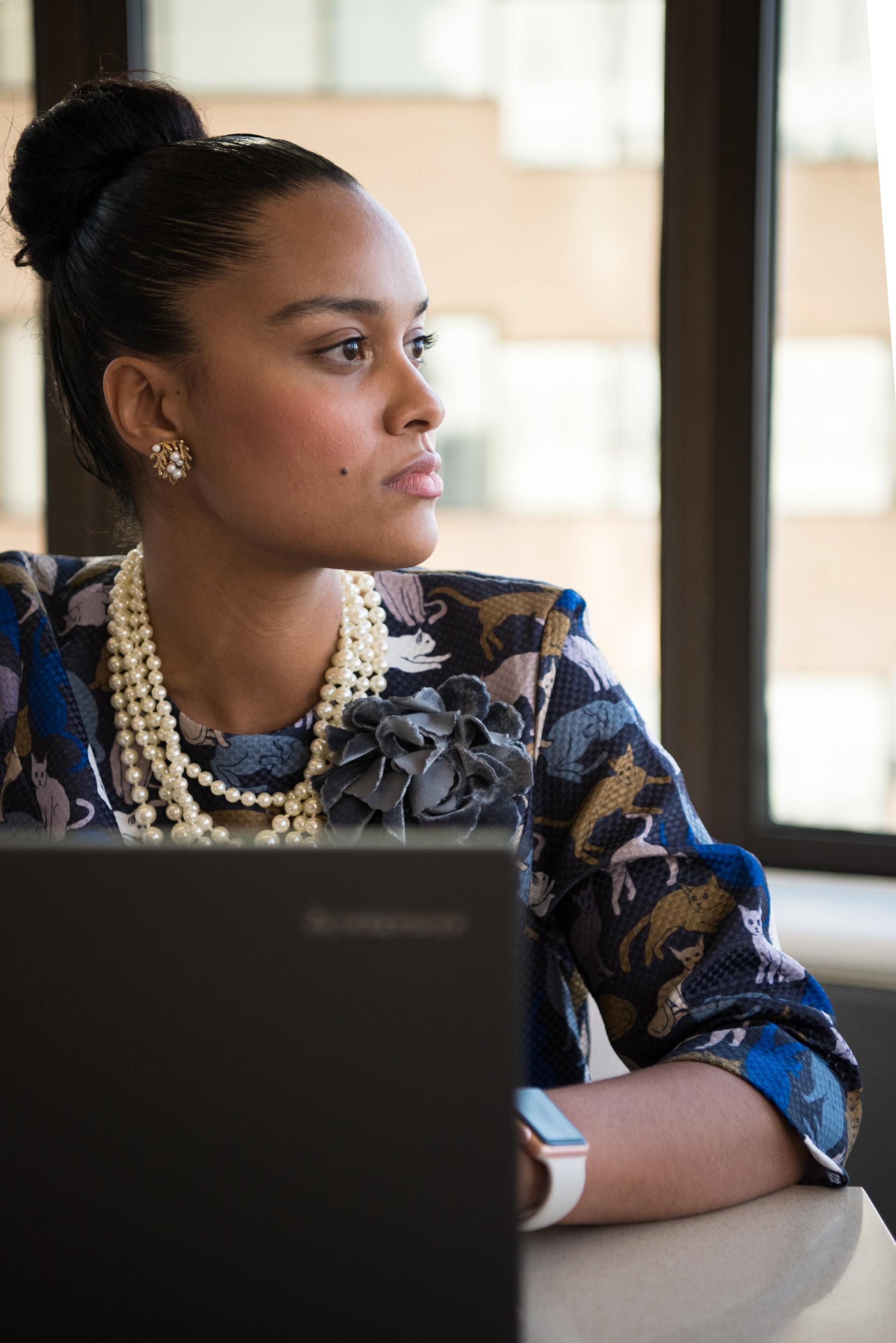 A woman is sitting in front of a laptop computer looking out a window.