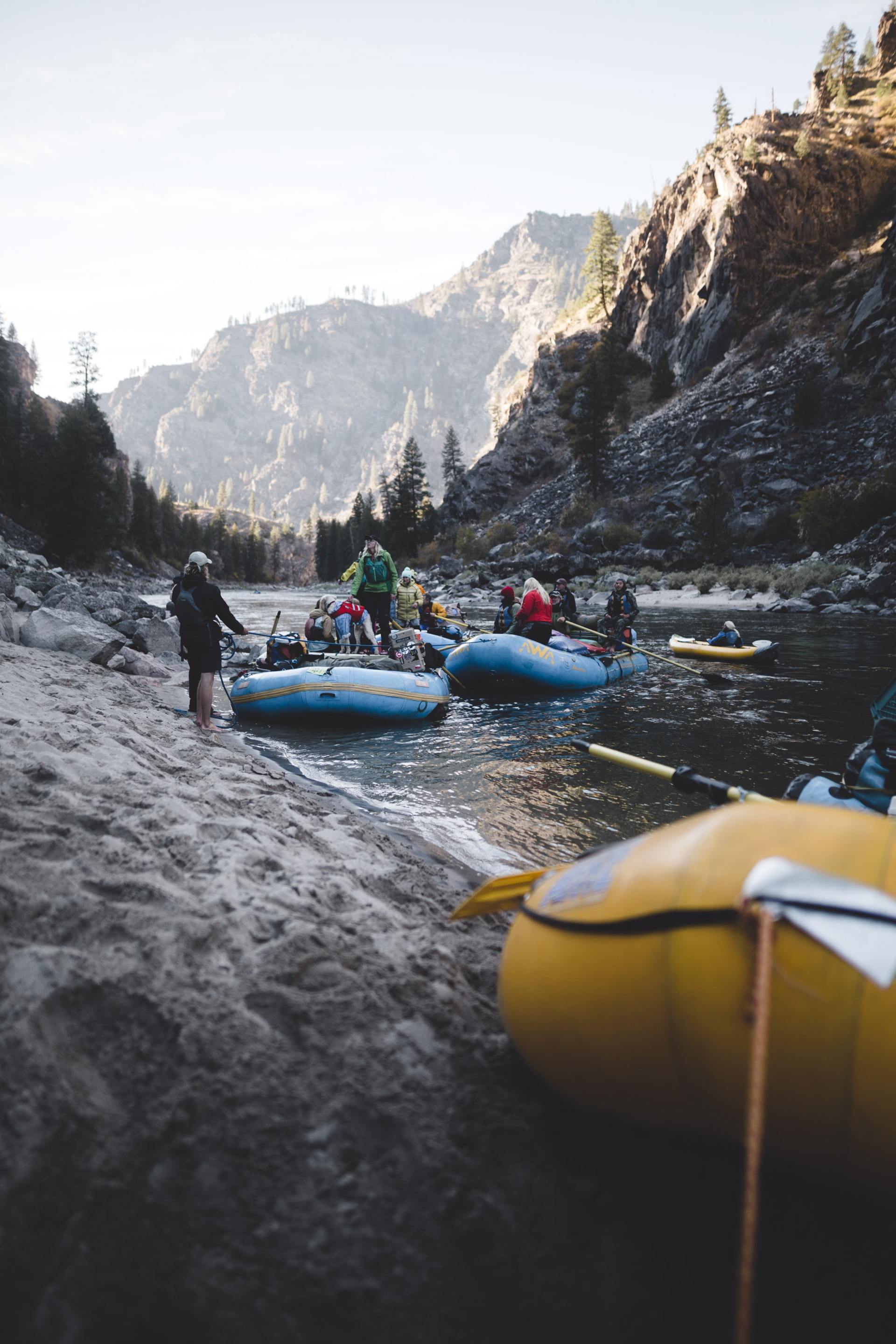 Raftinggruppe auf einem verschneiten Fluss unterhalb felsiger Canyonwände, im Vordergrund ein gelbes Floß