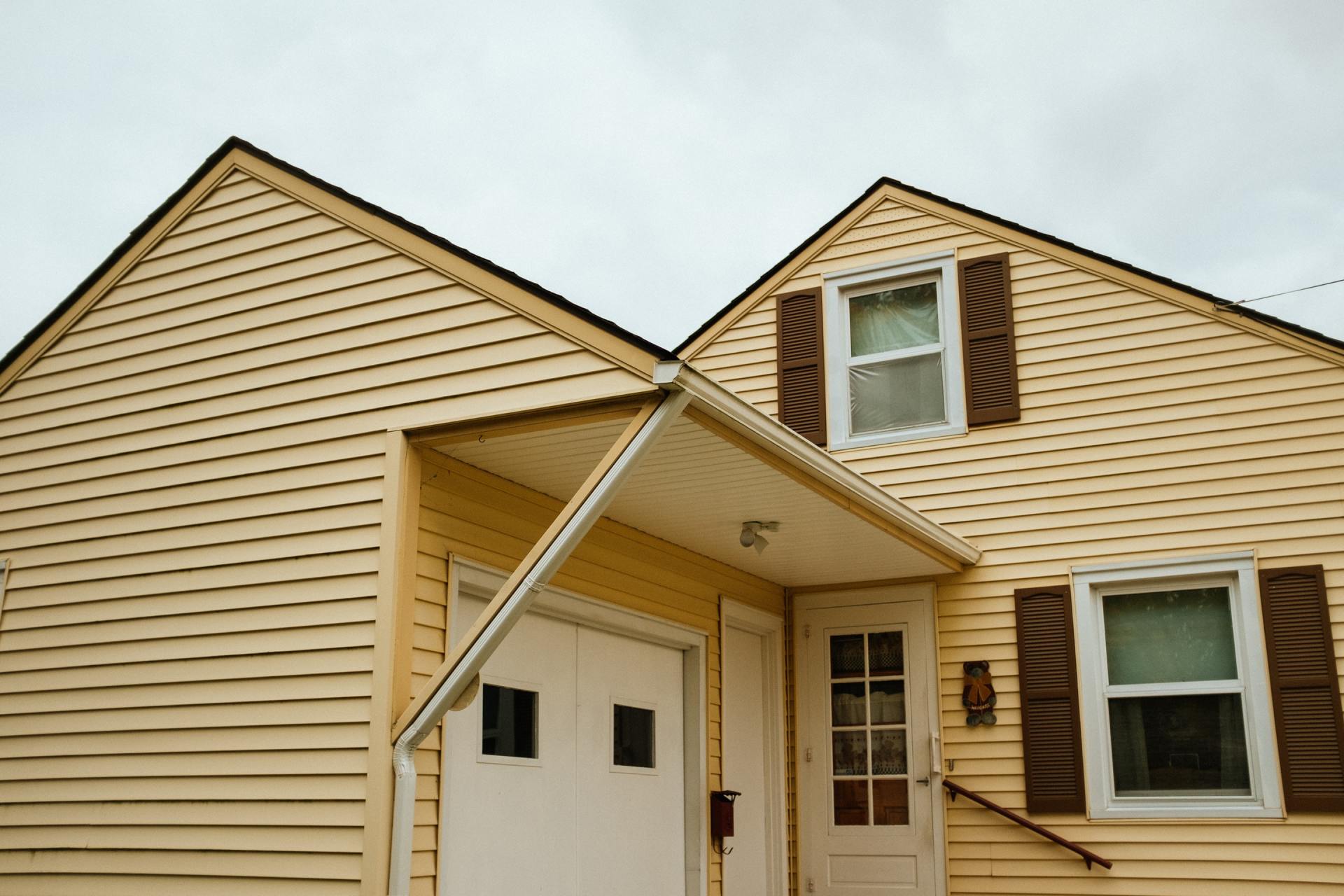A yellow house with a white garage door and brown shutters