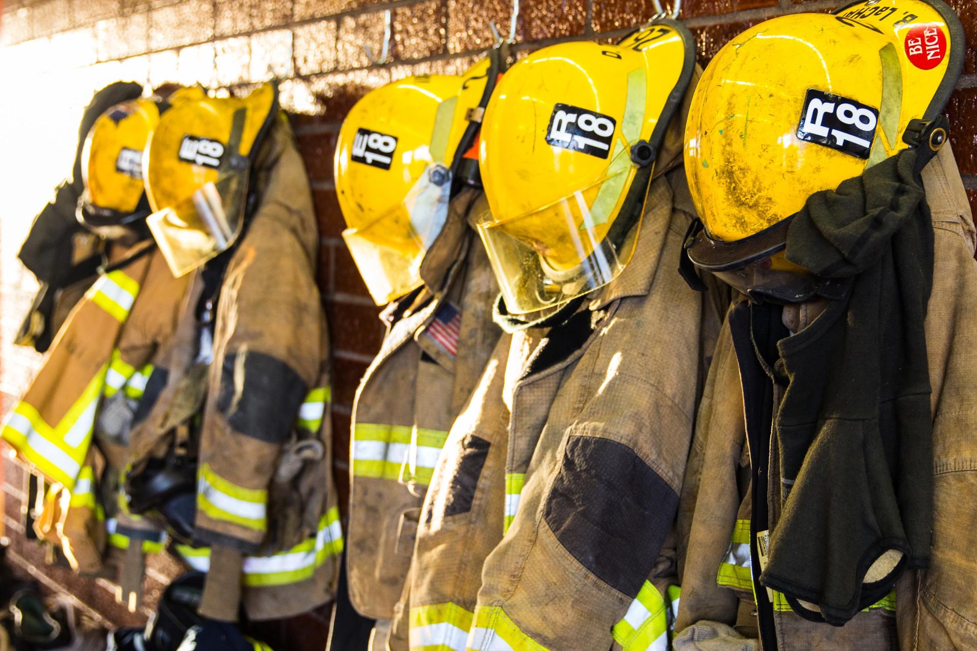 A row of firefighters wearing their uniforms and helmets hanging on a wall.