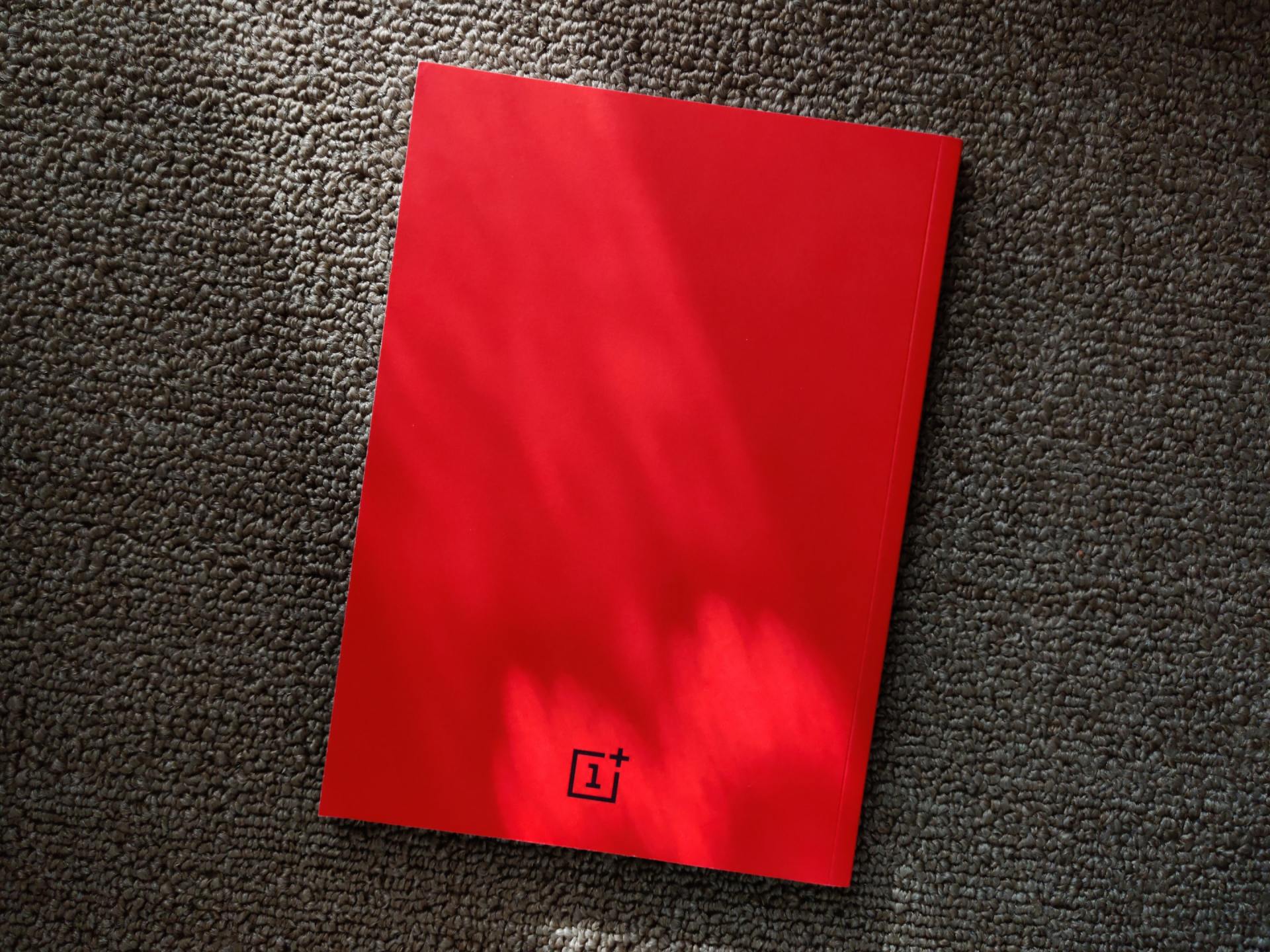 Een rood boek ligt op een zwart tapijt.
