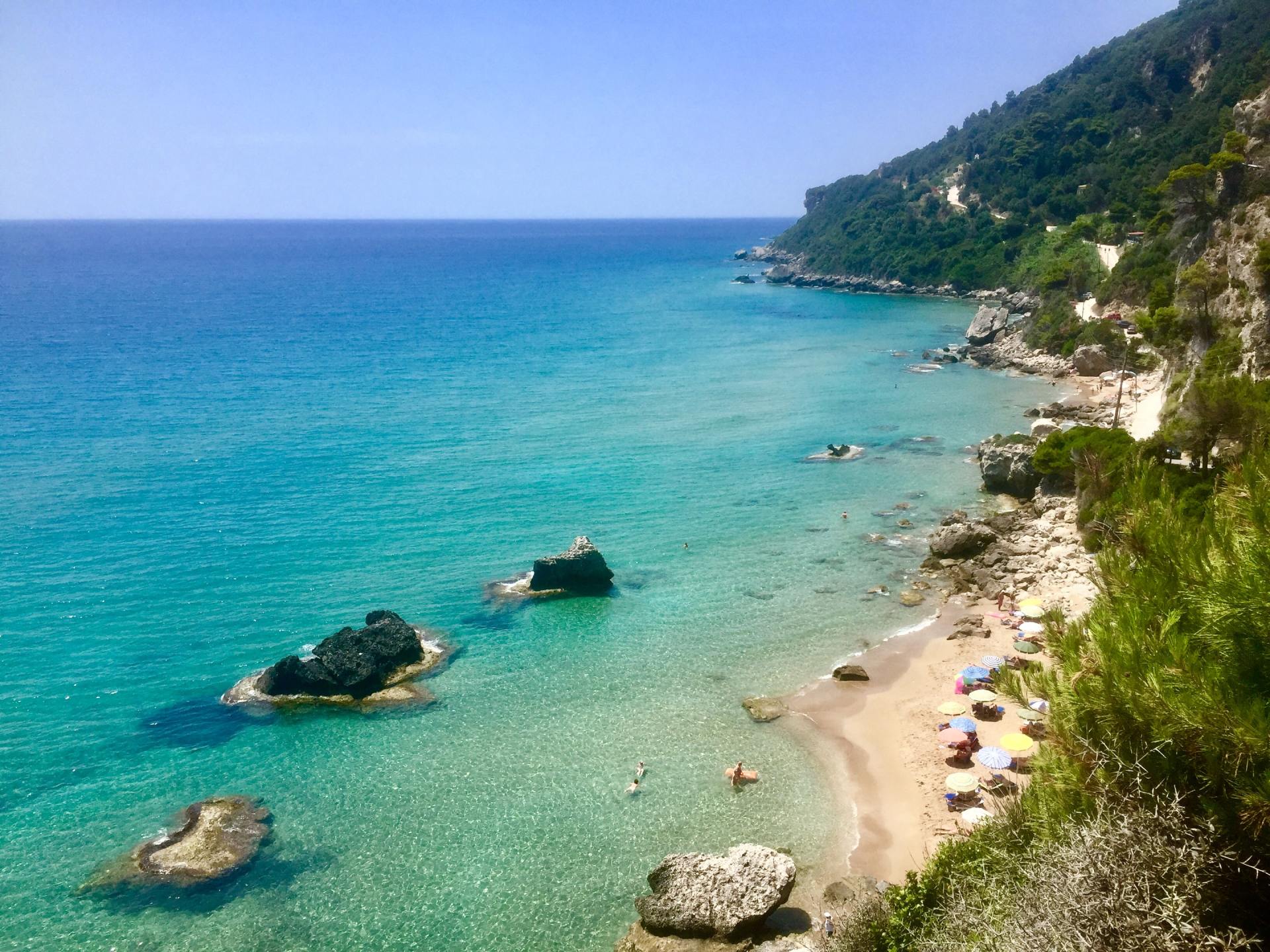 Kristallblaues Meer trifft auf Sandstrand und üppig grüne Hügel.