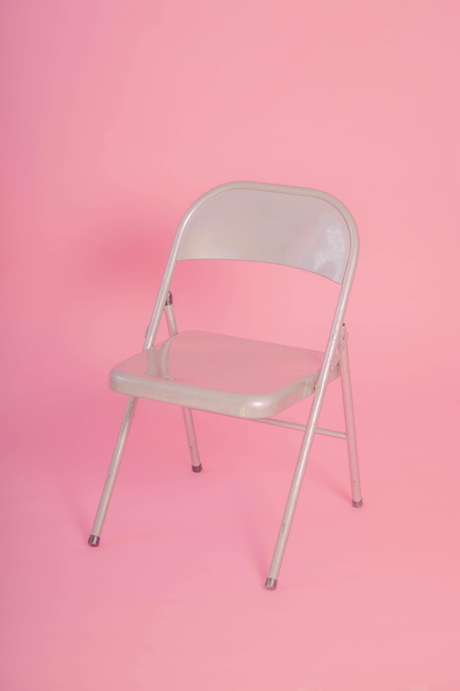 Una sedia pieghevole in metallo beige è posizionata al centro di uno sfondo rosa a tinta unita.