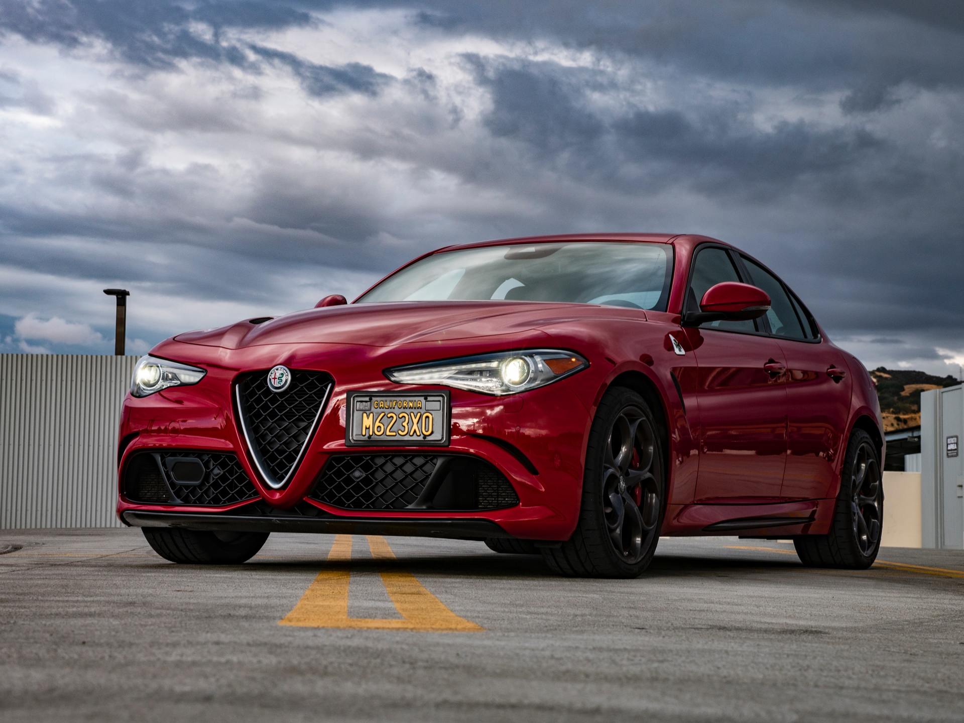 Red Alfa Romeo Giulia parked on a rooftop, overcast sky.