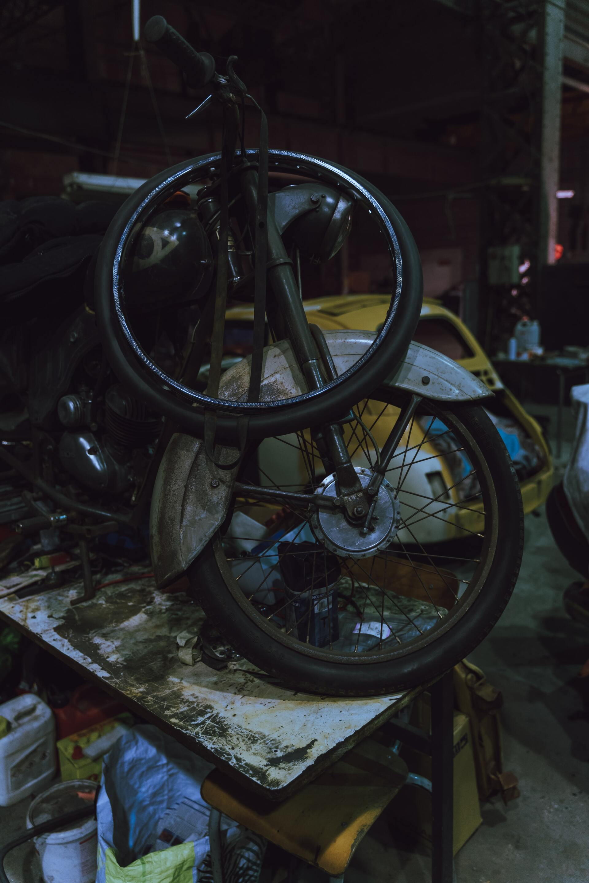 Vintage motorcycle with a spare wheel propped on a workbench in a dimly lit garage.
