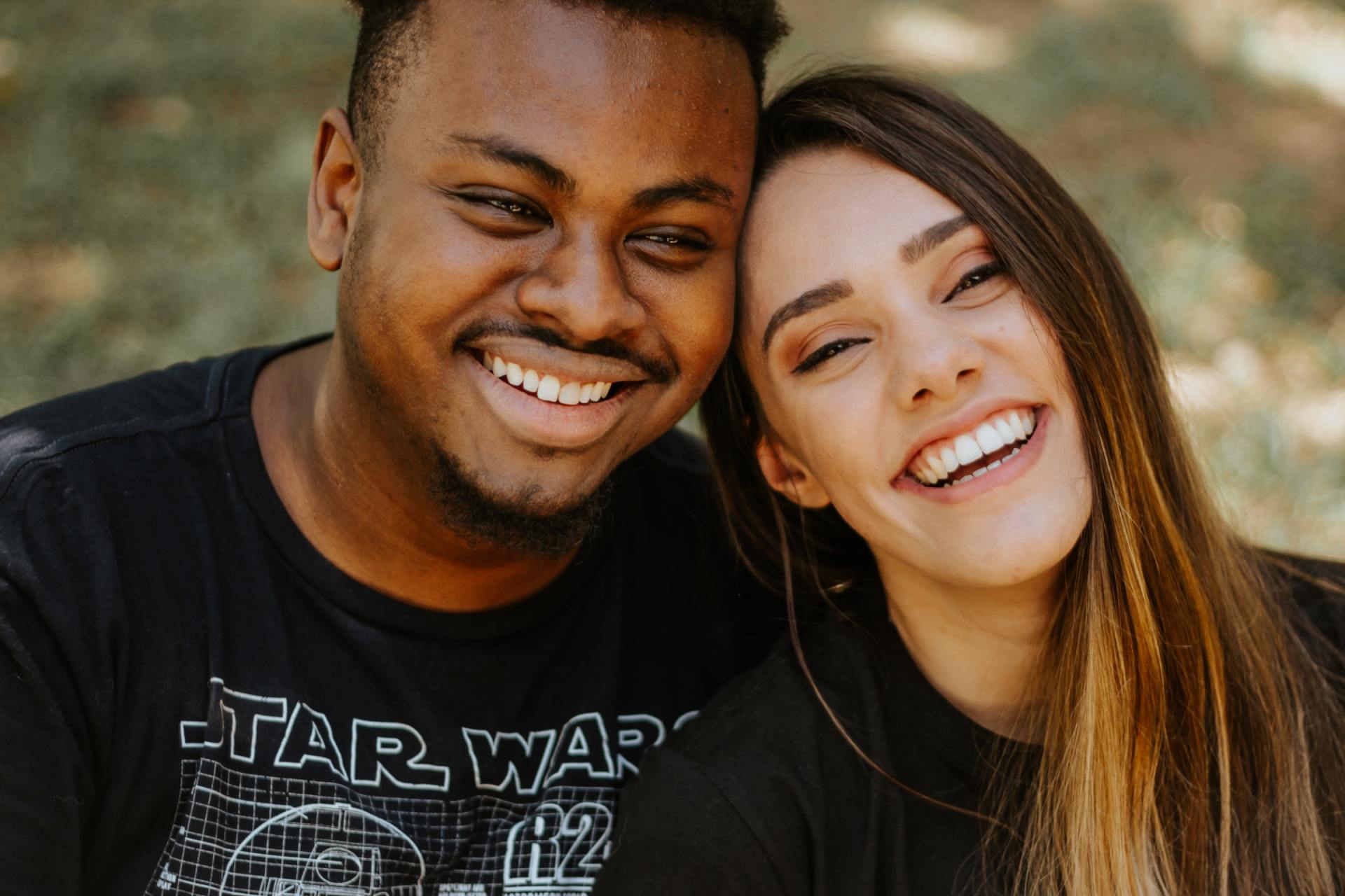 A man and a woman are smiling for the camera . the man is wearing a star wars shirt.