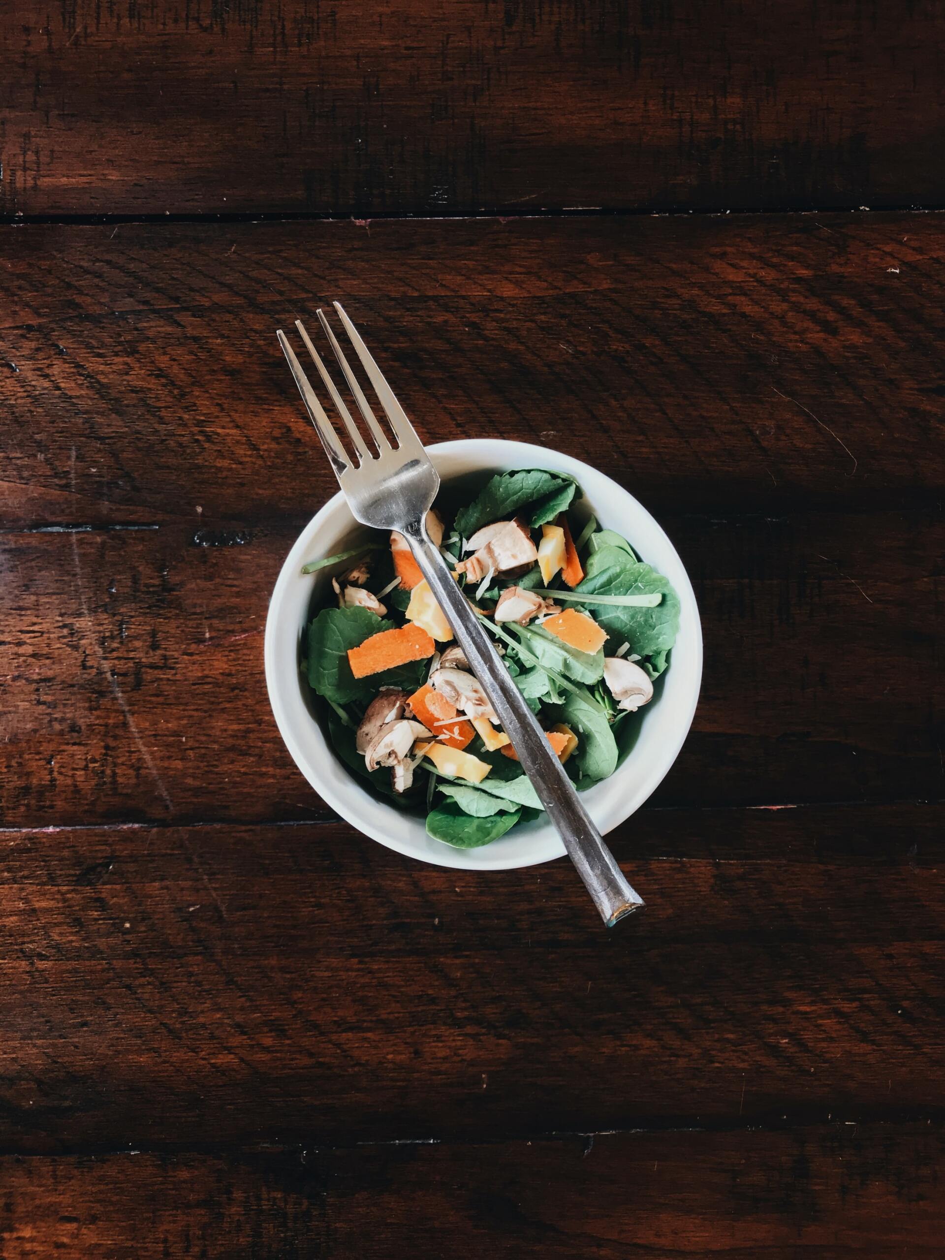 Salad in a white bowl with a fork on a dark wooden table.