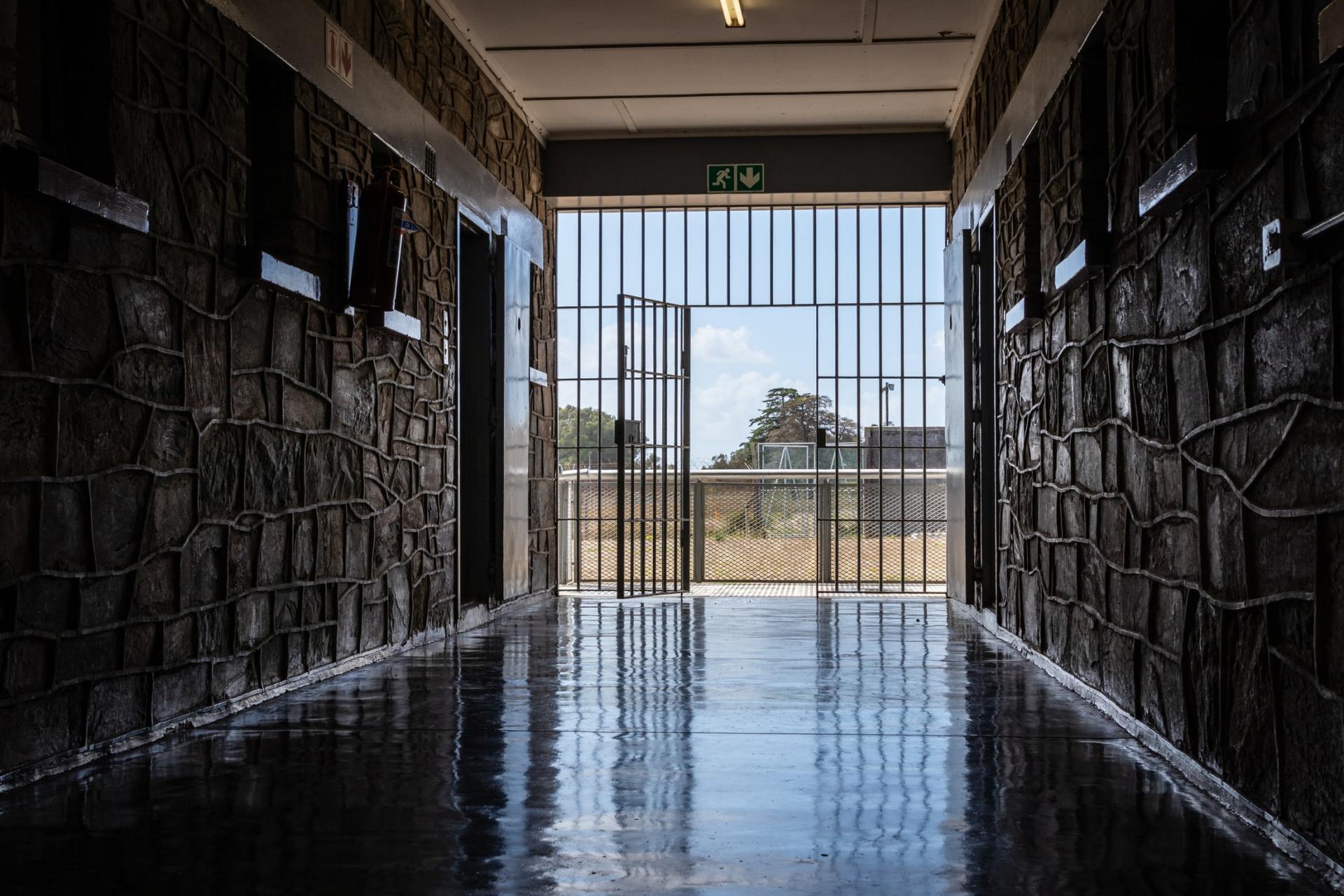 A long hallway in a prison with a prison cell door open.