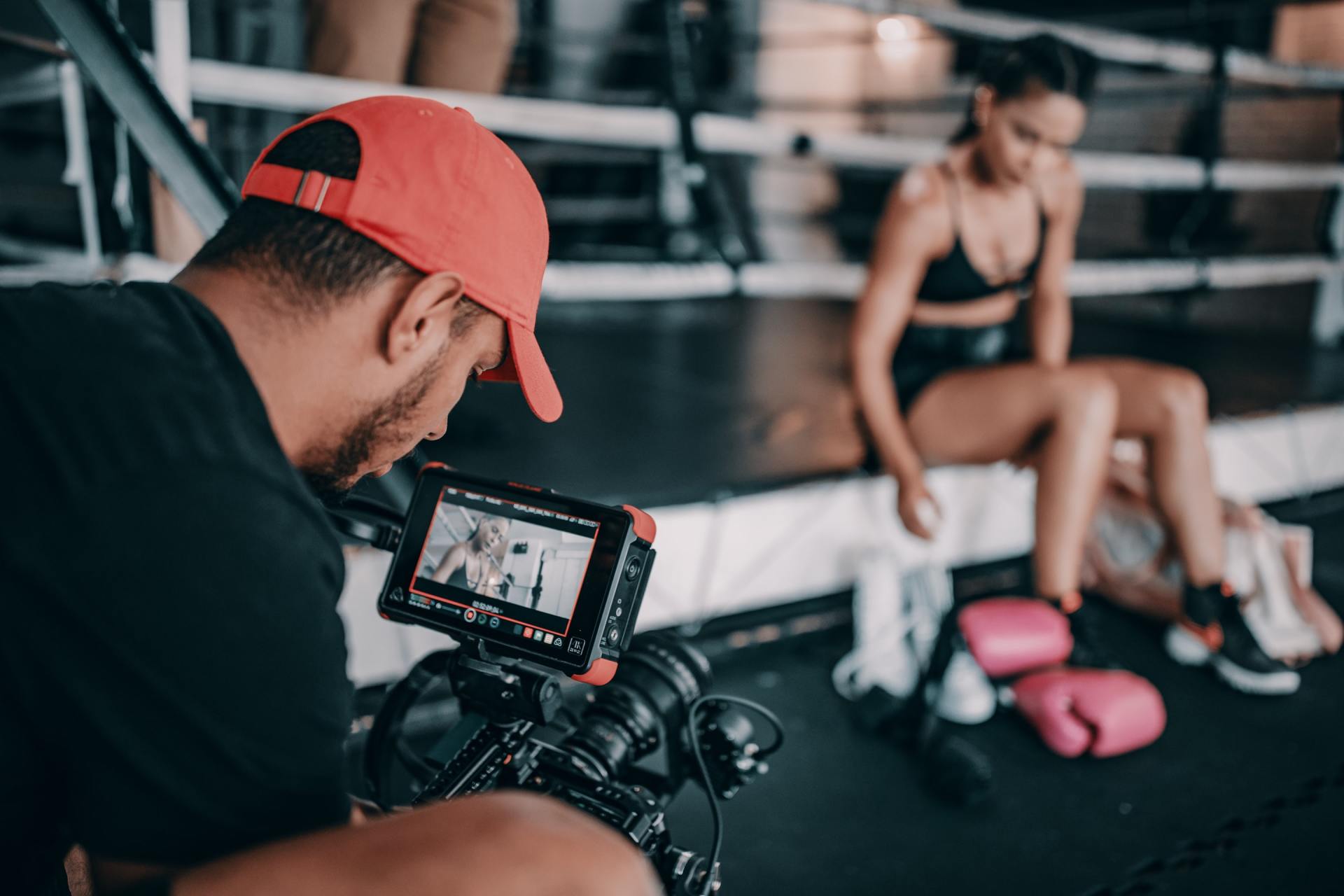 Camera filming a woman resting in a gym beside pink boxing gloves