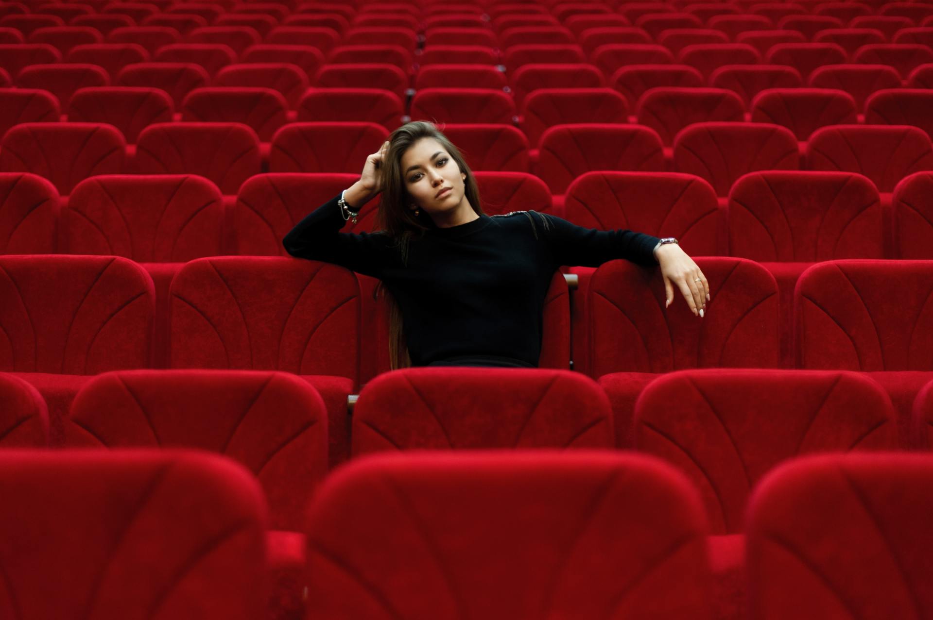 Una mujer está sentada en un auditorio vacío con asientos rojos.