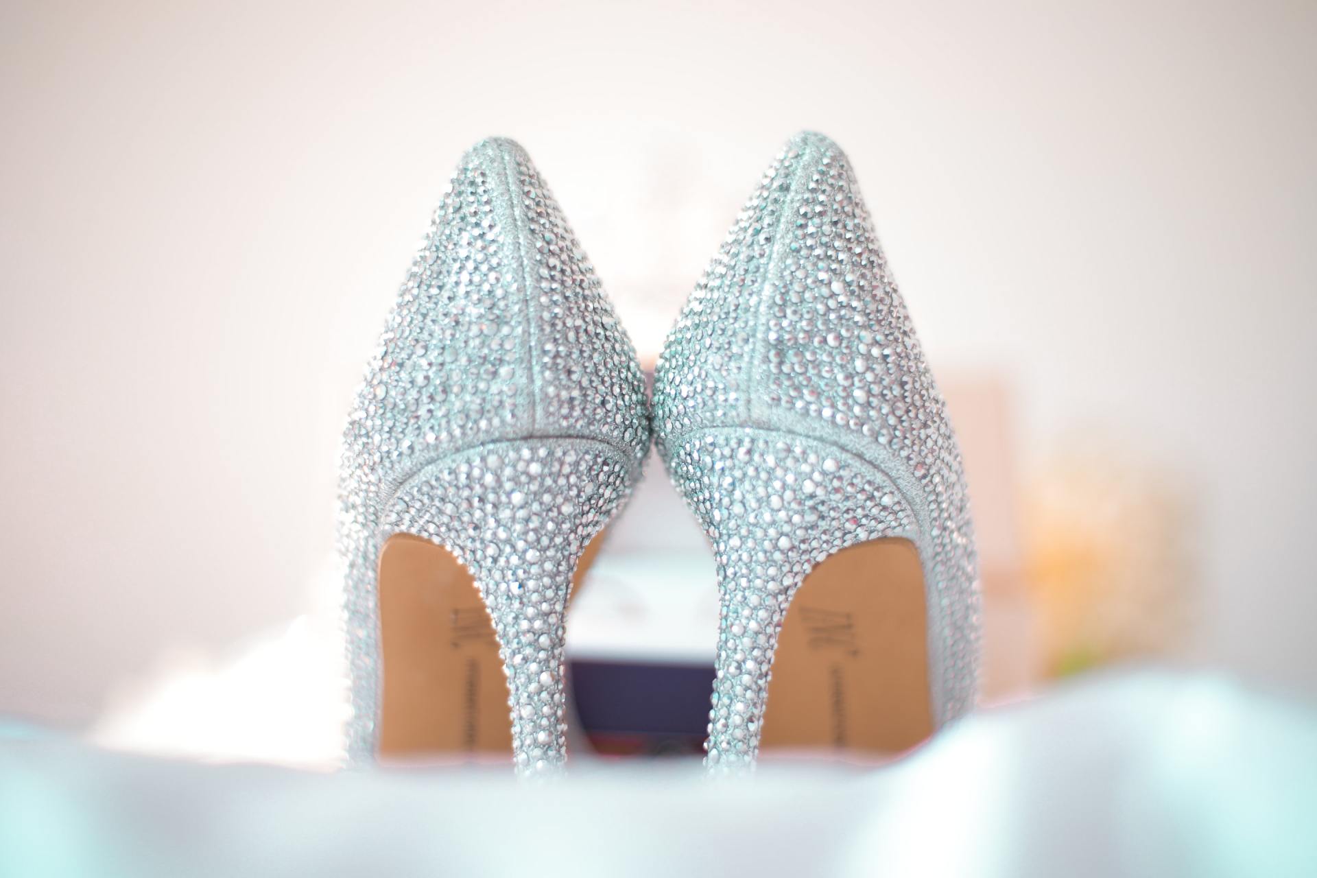 A pair of silver high heels are sitting on a bed.
