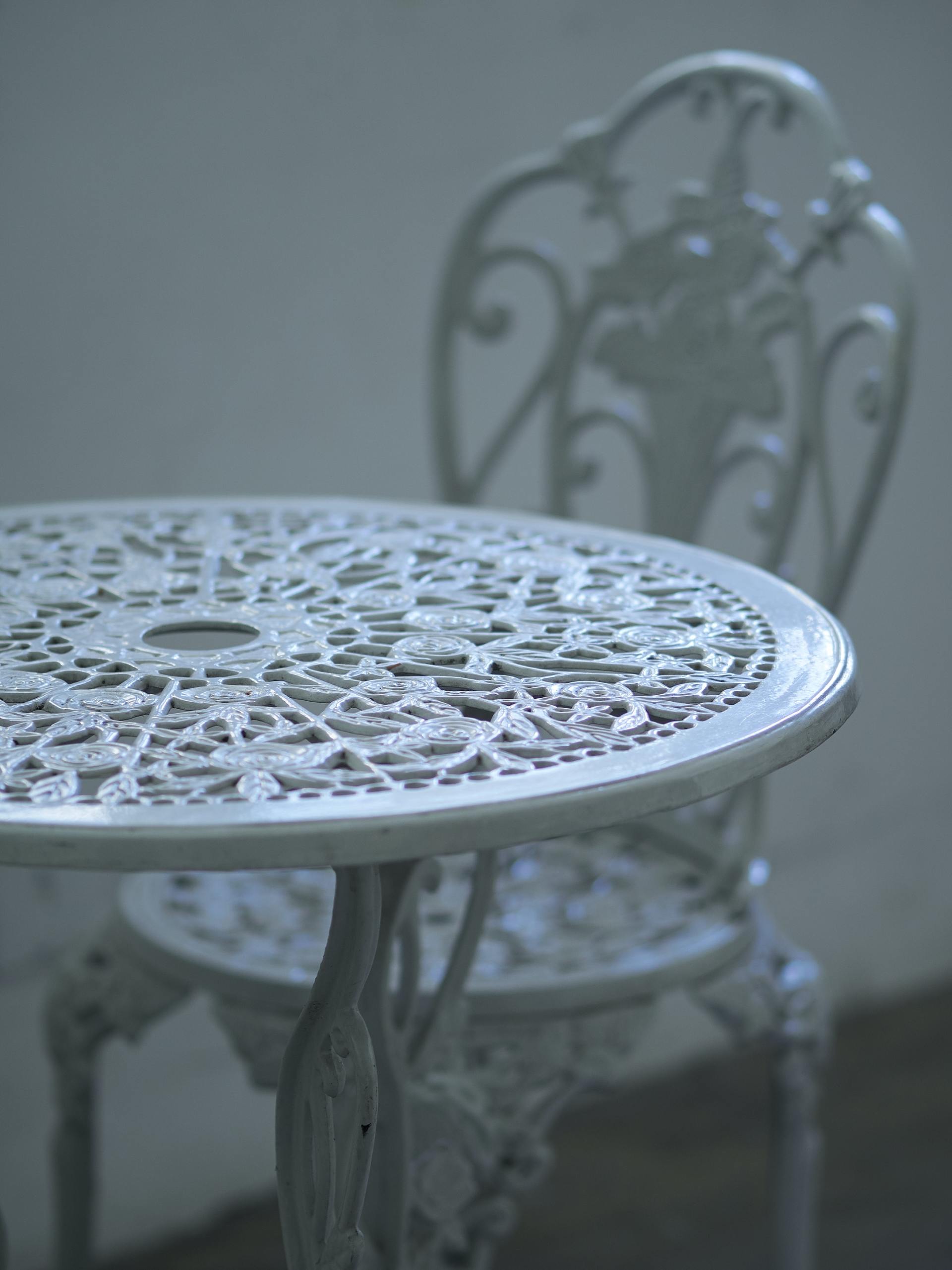 Un set da bistrot da esterno in metallo bianco e decorato, con un tavolo circolare con un intricato motivo a griglia e una sedia abbinata.
