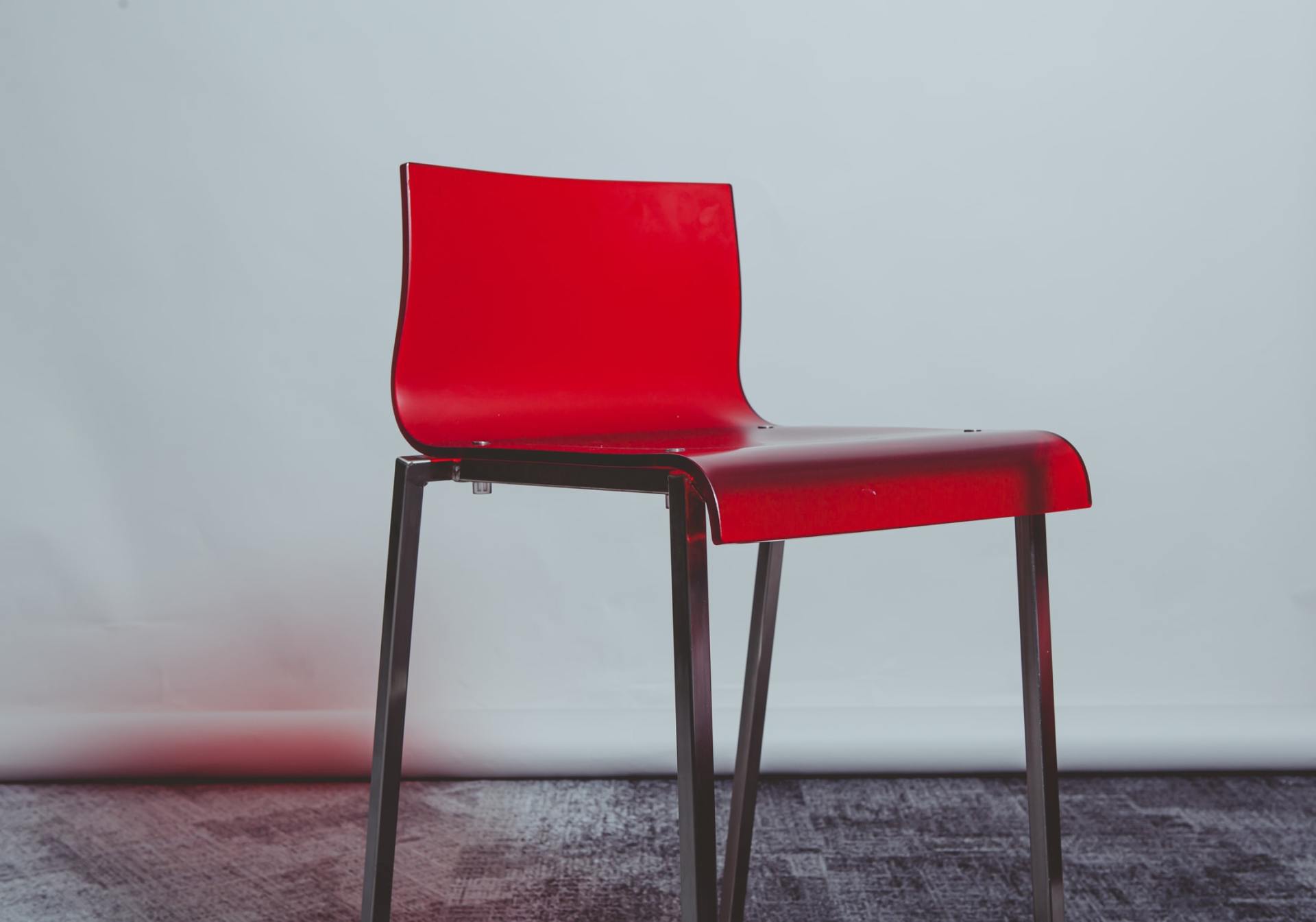 Una sedia rossa e minimalista con uno schienale elegante e sottili gambe in metallo, su uno sfondo semplice grigio chiaro.