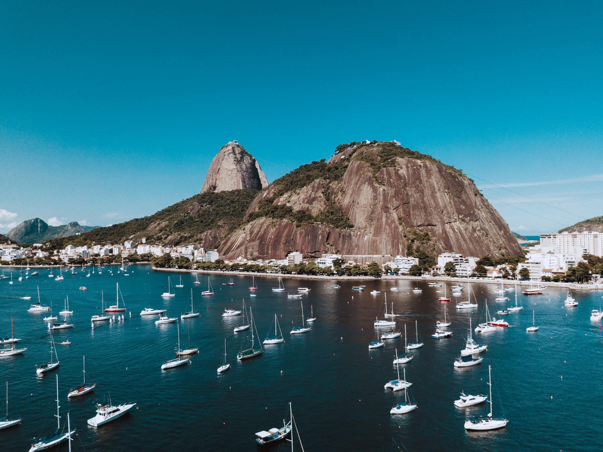 Vista aérea do Pão de Açúcar no Rio de Janeiro, com vários barcos ancorados nas águas azuis em primeiro plano.