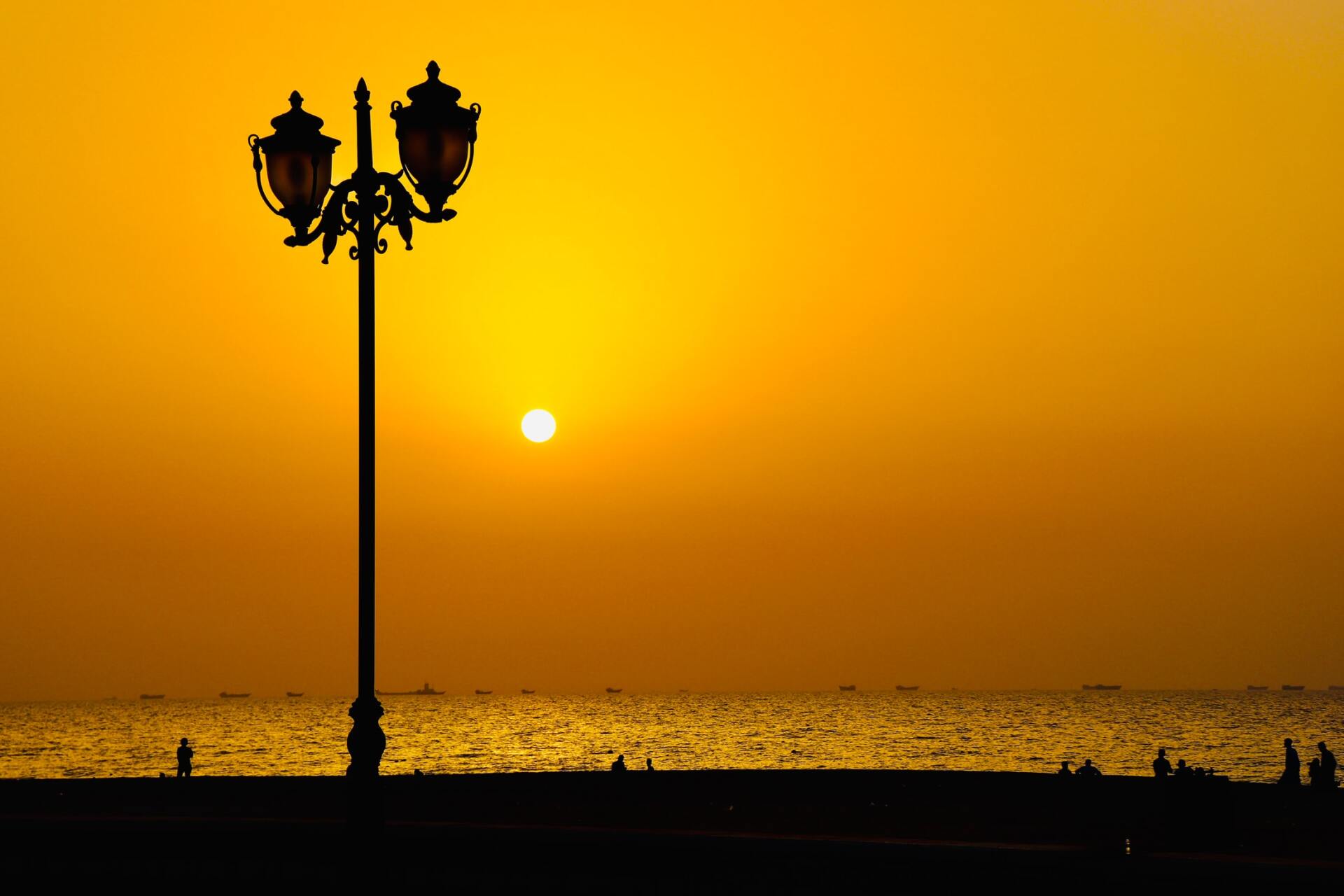 Die Silhouette einer Straßenlaterne zeichnet sich vor dem Sonnenuntergang über dem Meer ab.