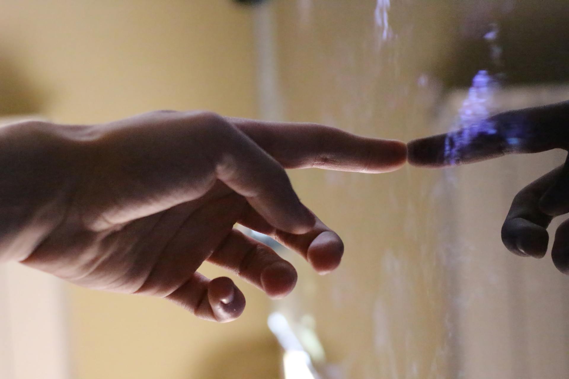 Two hands, one light-skinned, the other dark, touching through a clear surface.