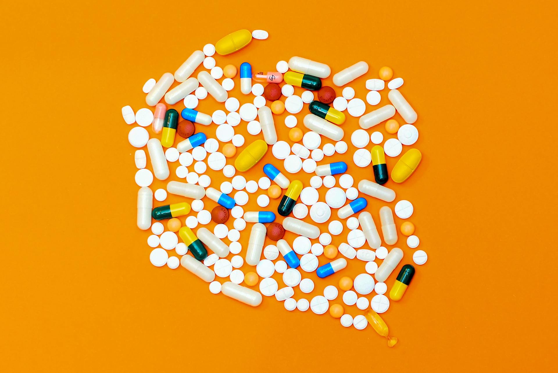 A pile of pills and capsules on an orange background.