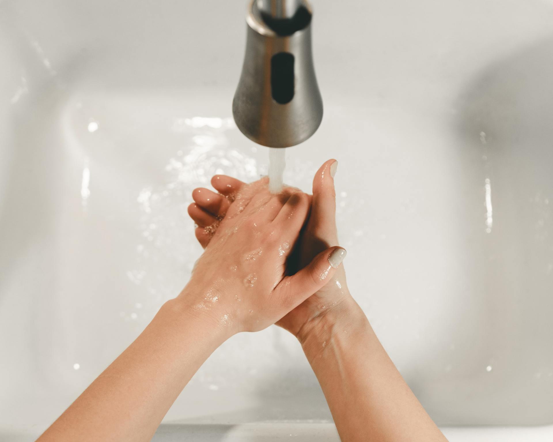 Een persoon wast zijn handen onder een kraan met water