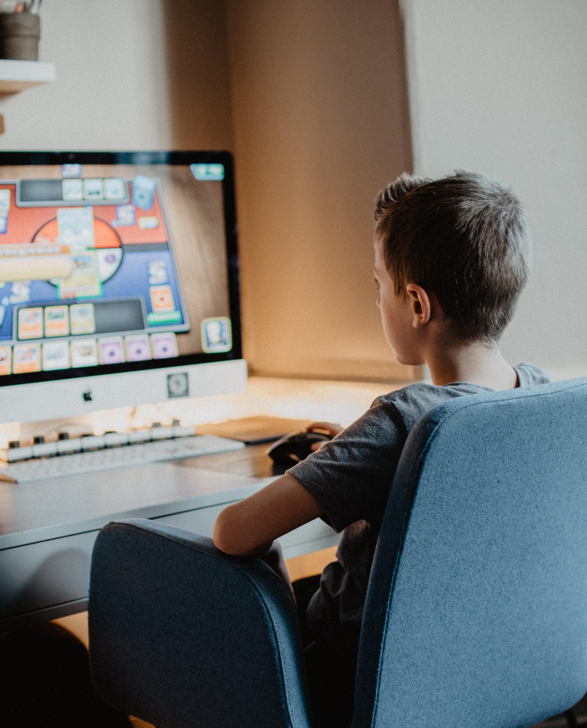 A young boy is sitting in front of an apple computer playing a game.