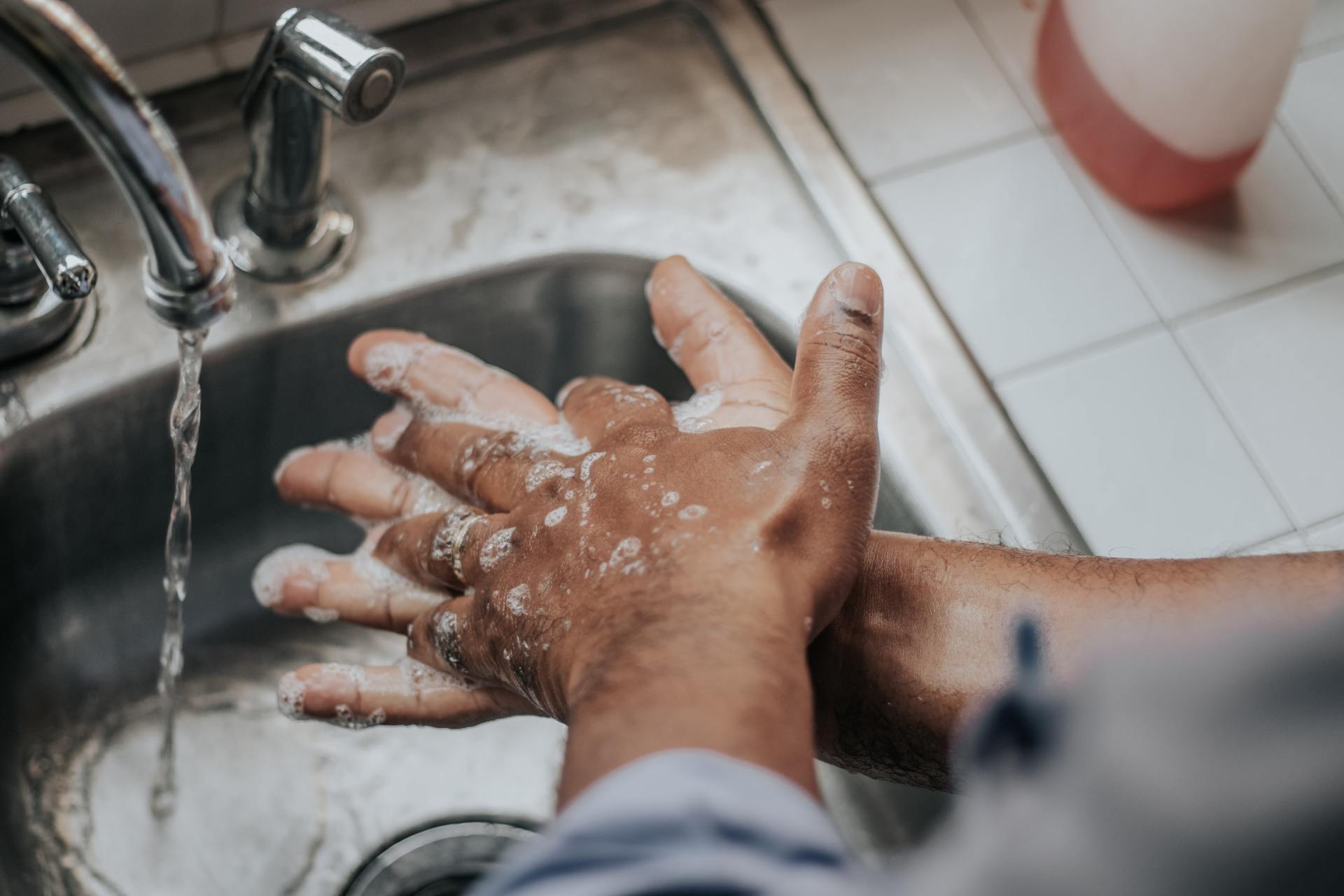 Hands lathered with soap under running water in a sink.