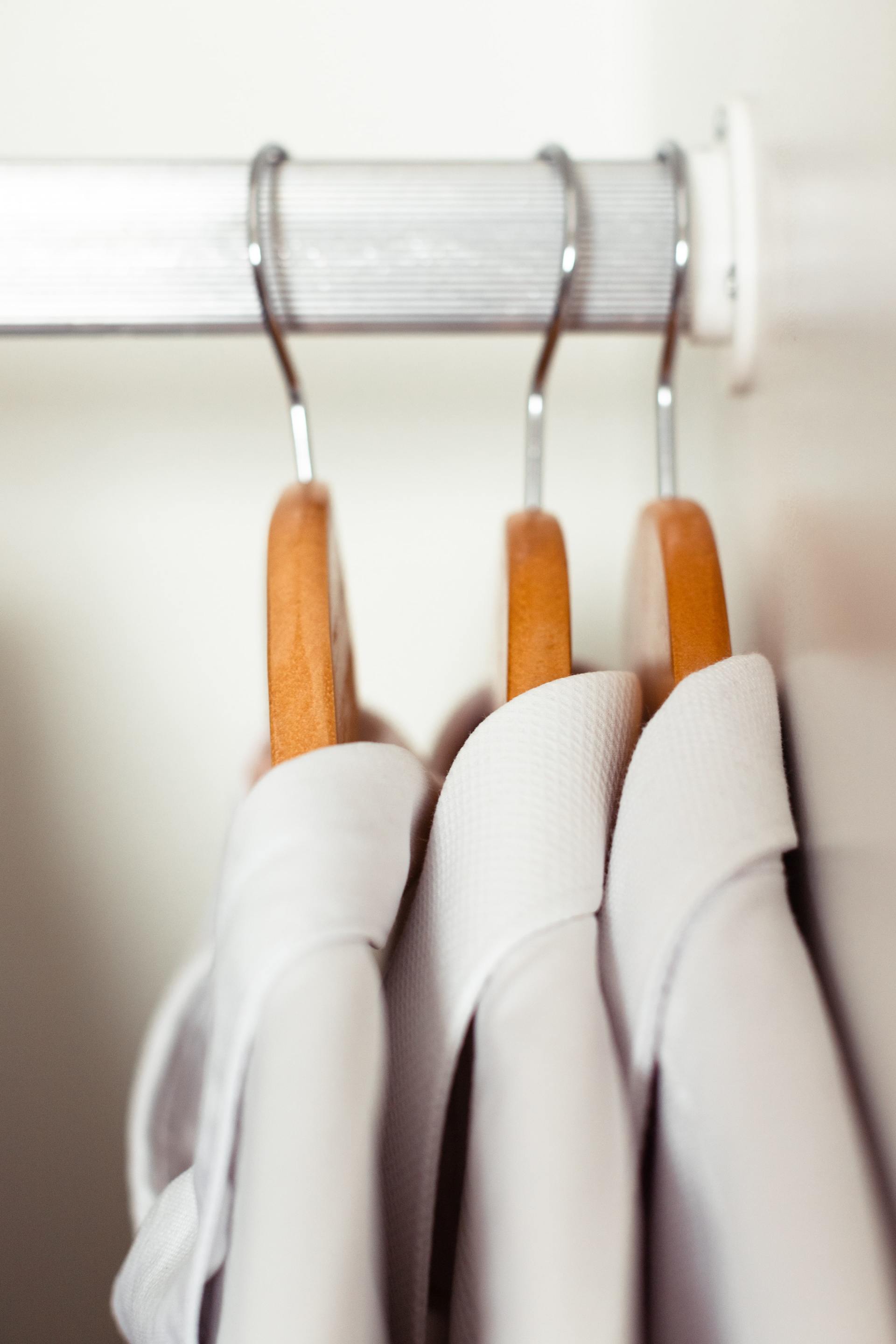 Witte overhemden hangen aan houten hangers aan een witte kledingroede in de kast.