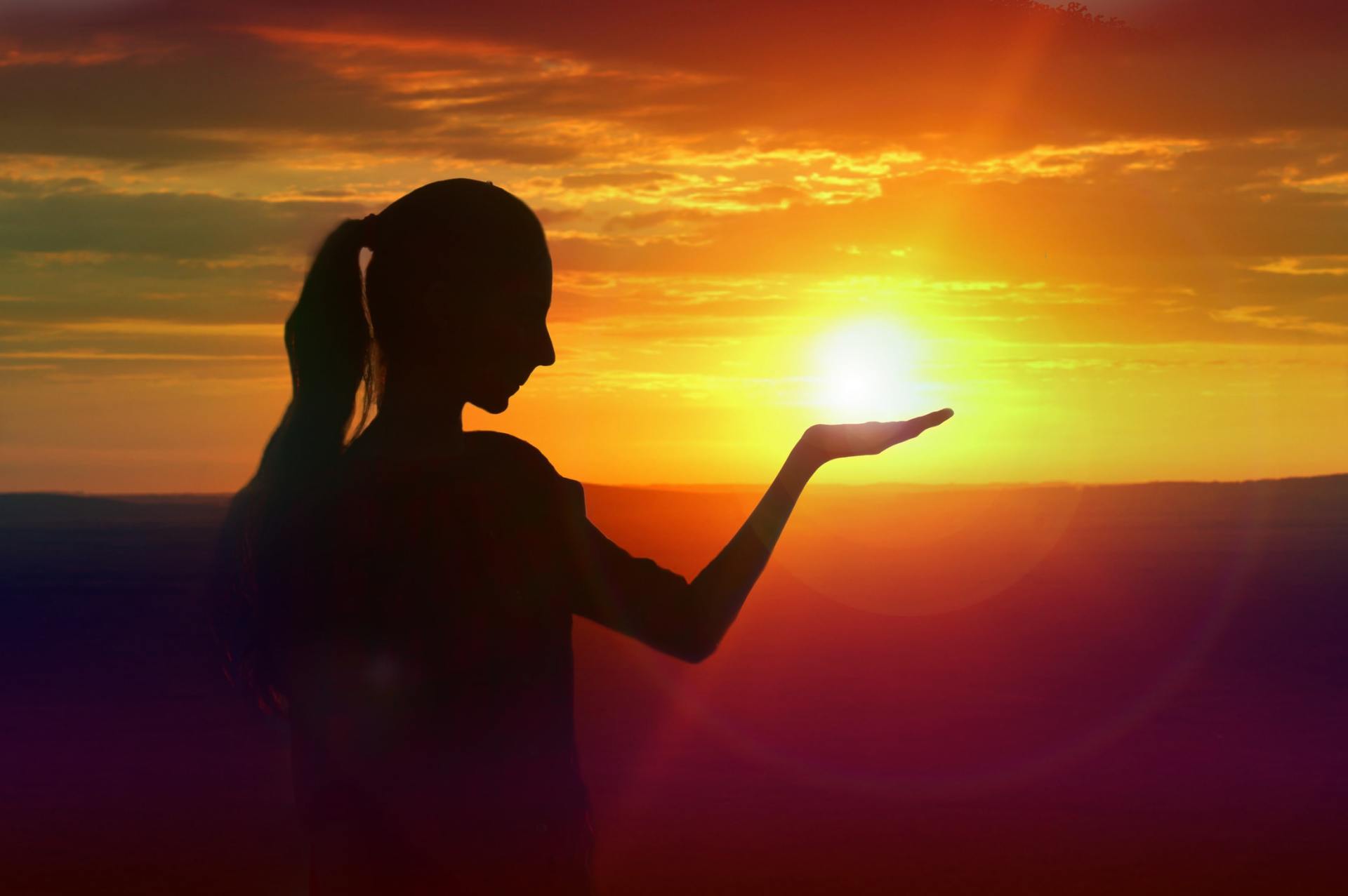A woman is holding the sun in her hand at sunset.