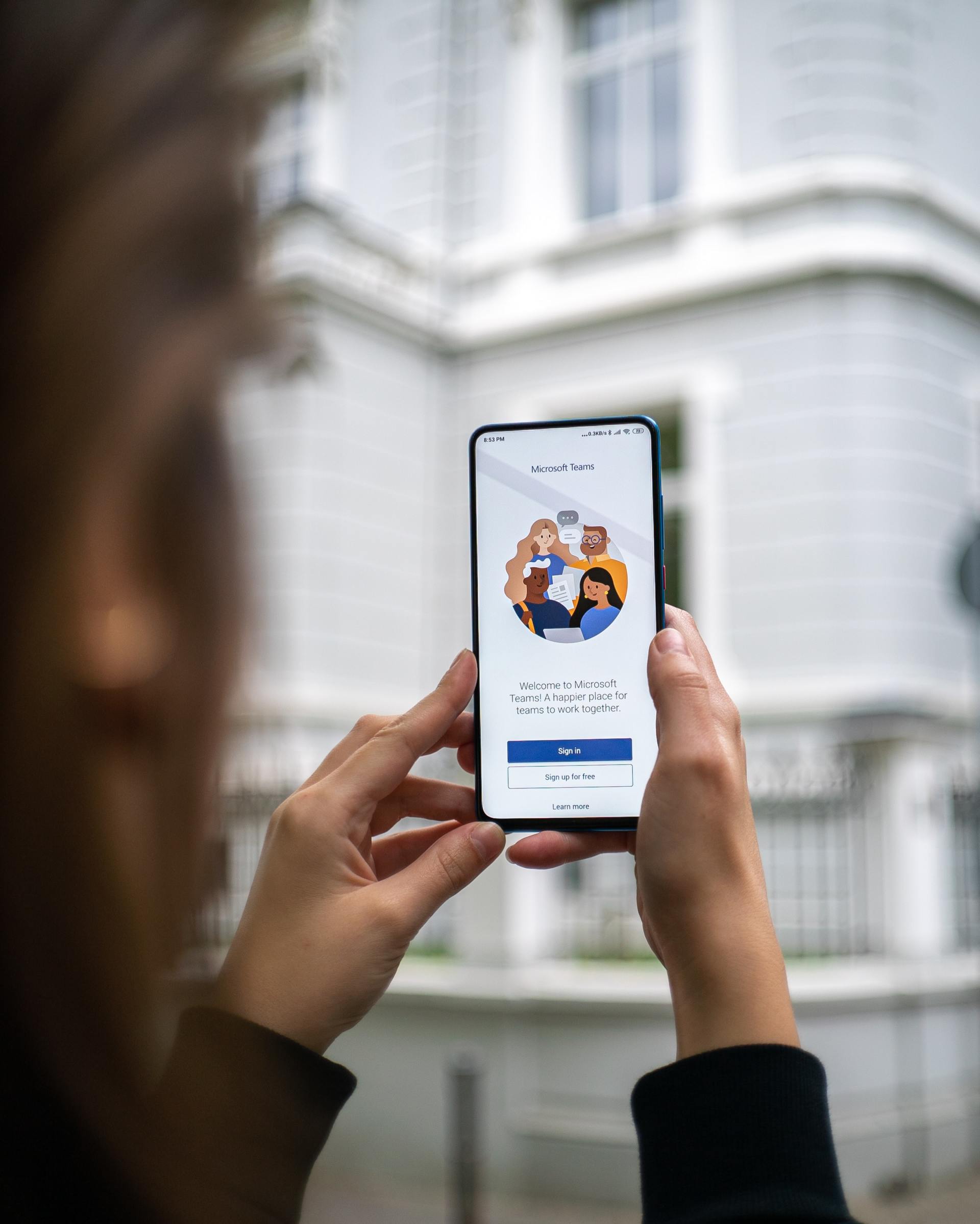 A woman is holding a cell phone in her hands in front of a building.