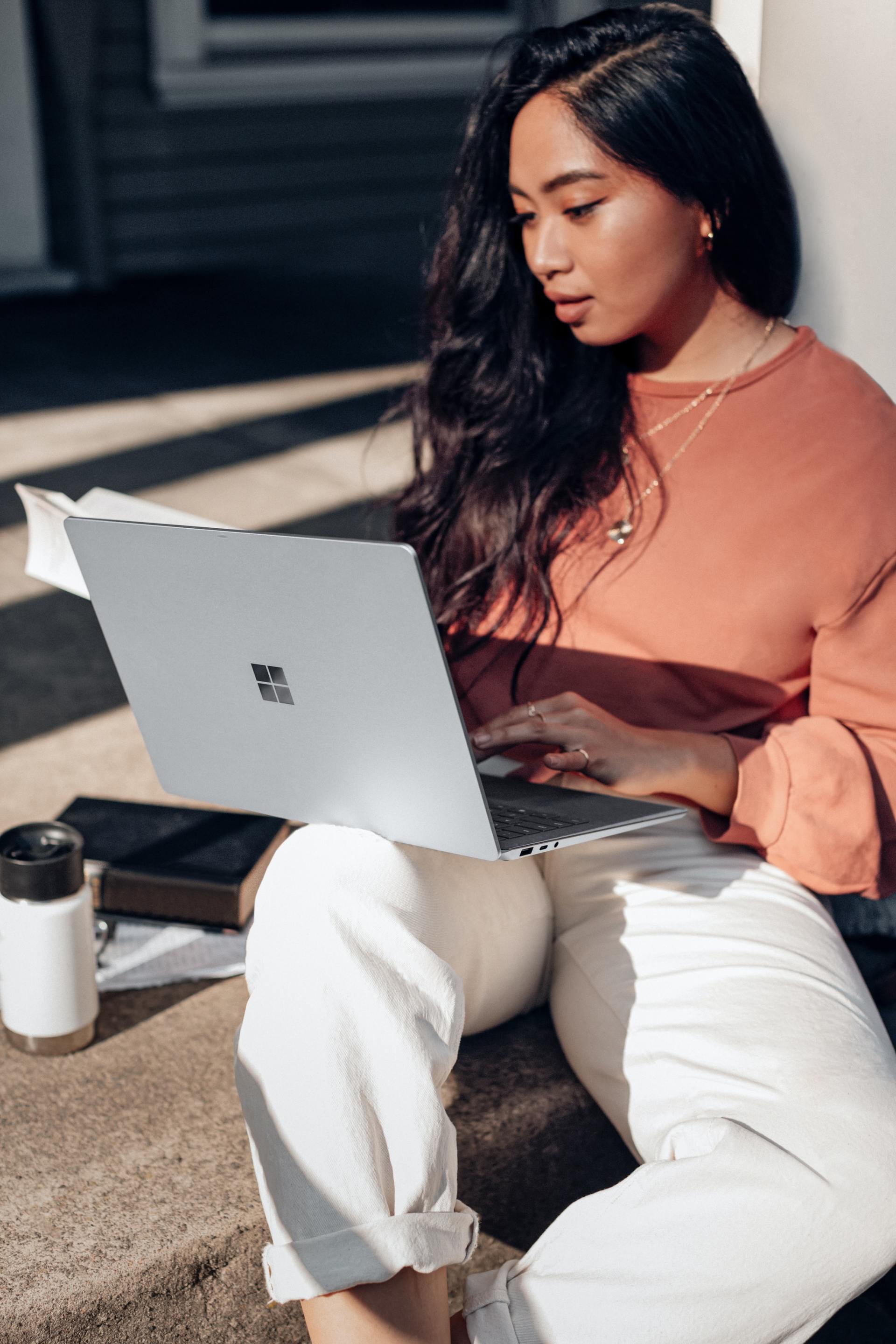 Una mujer está sentada en un escalón usando una computadora portátil.