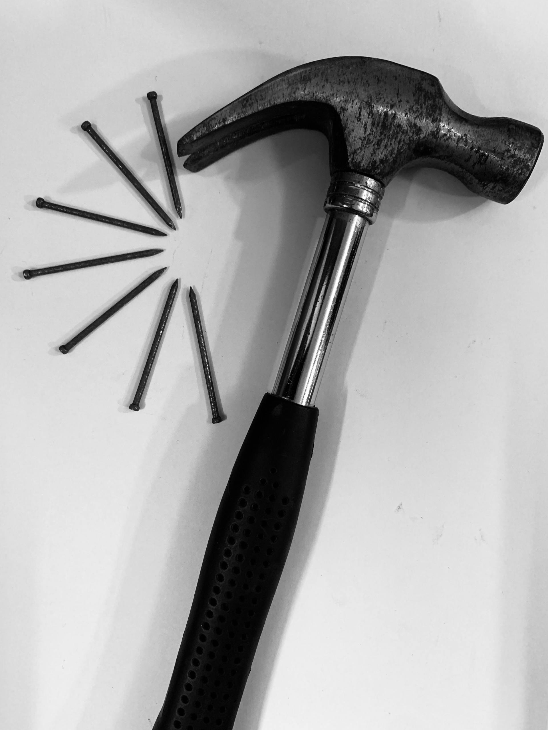 Hammer with nails fanned out on a white surface.
