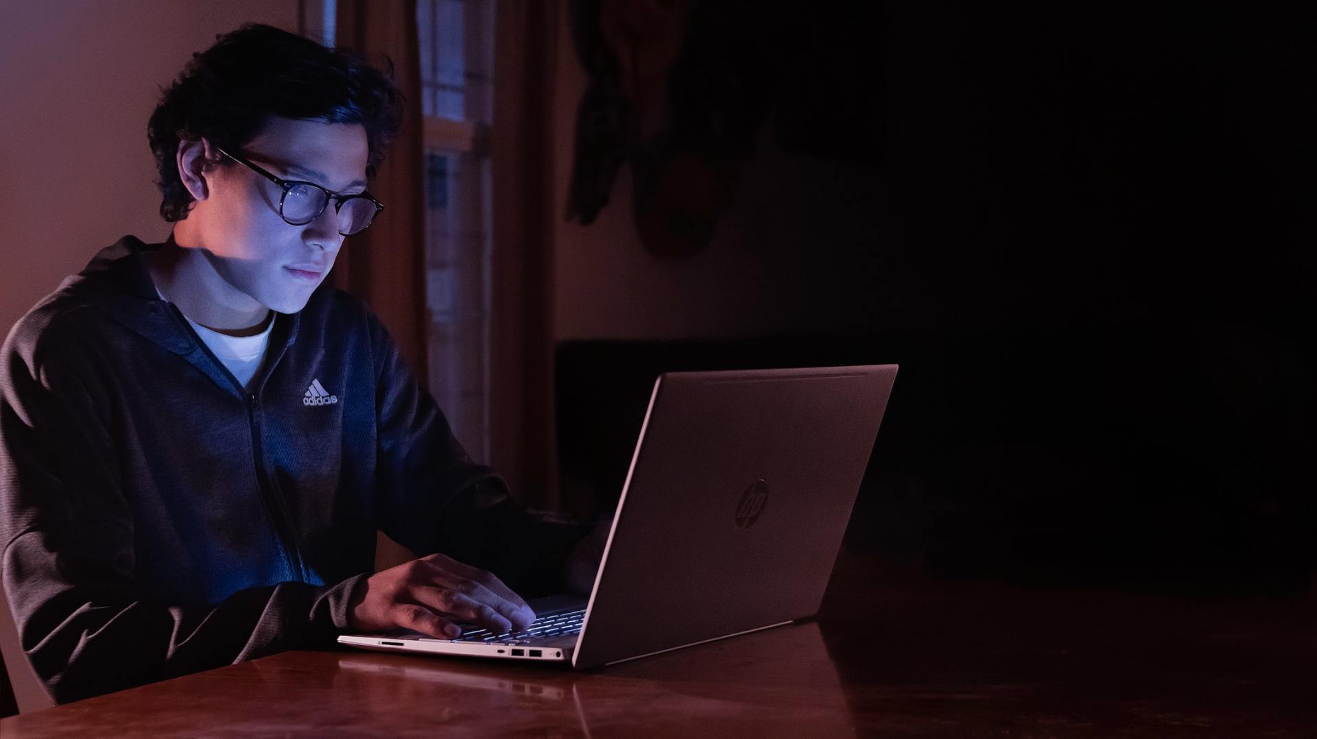 Persona tecleando en un ordenador portátil en un escritorio con poca luz, iluminado por la pantalla.