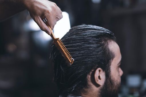 Person having hair styled with a comb; hands of stylist applying product.