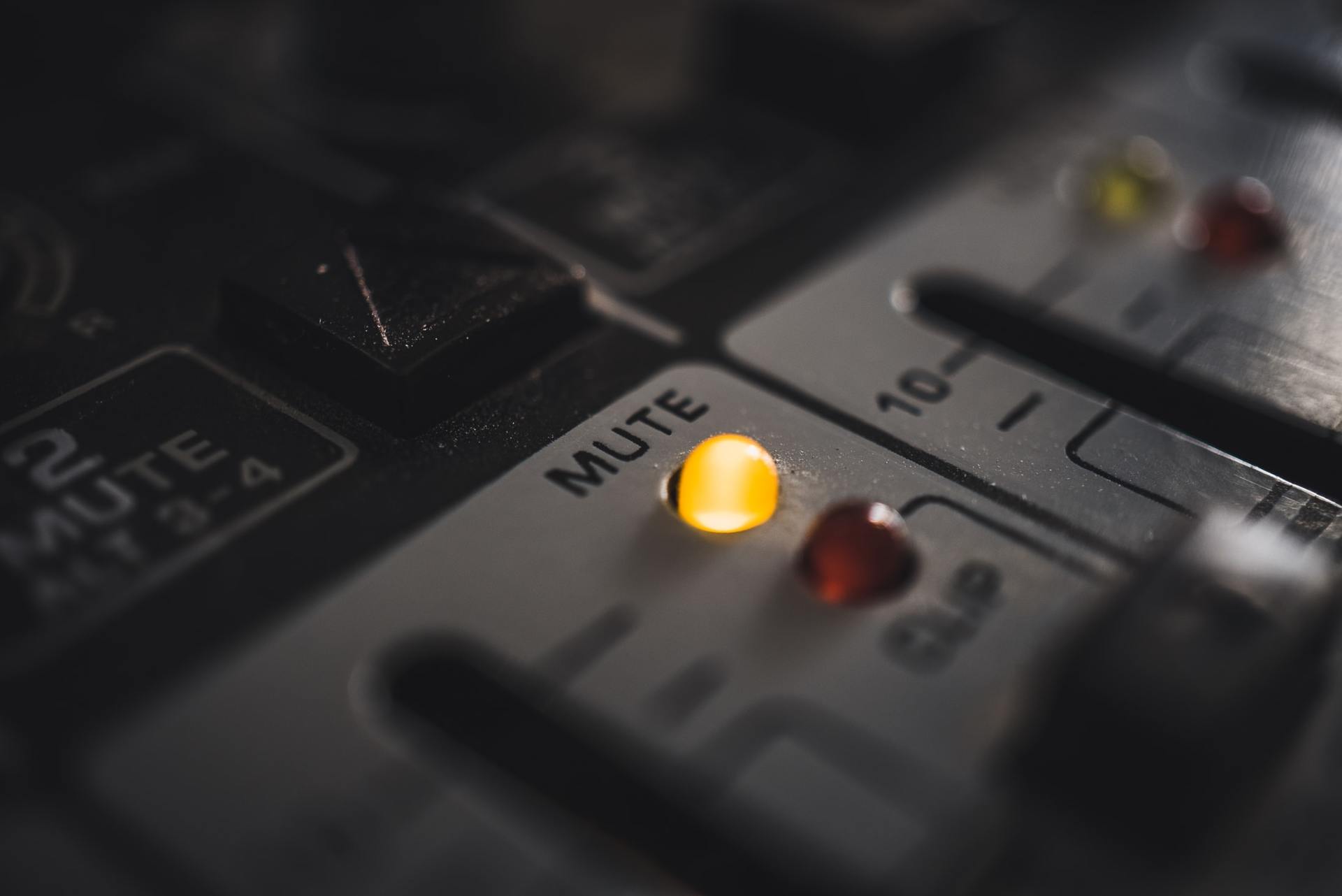 Close-up of a gray audio mixer panel with an illuminated yellow mute button and red indicator lights