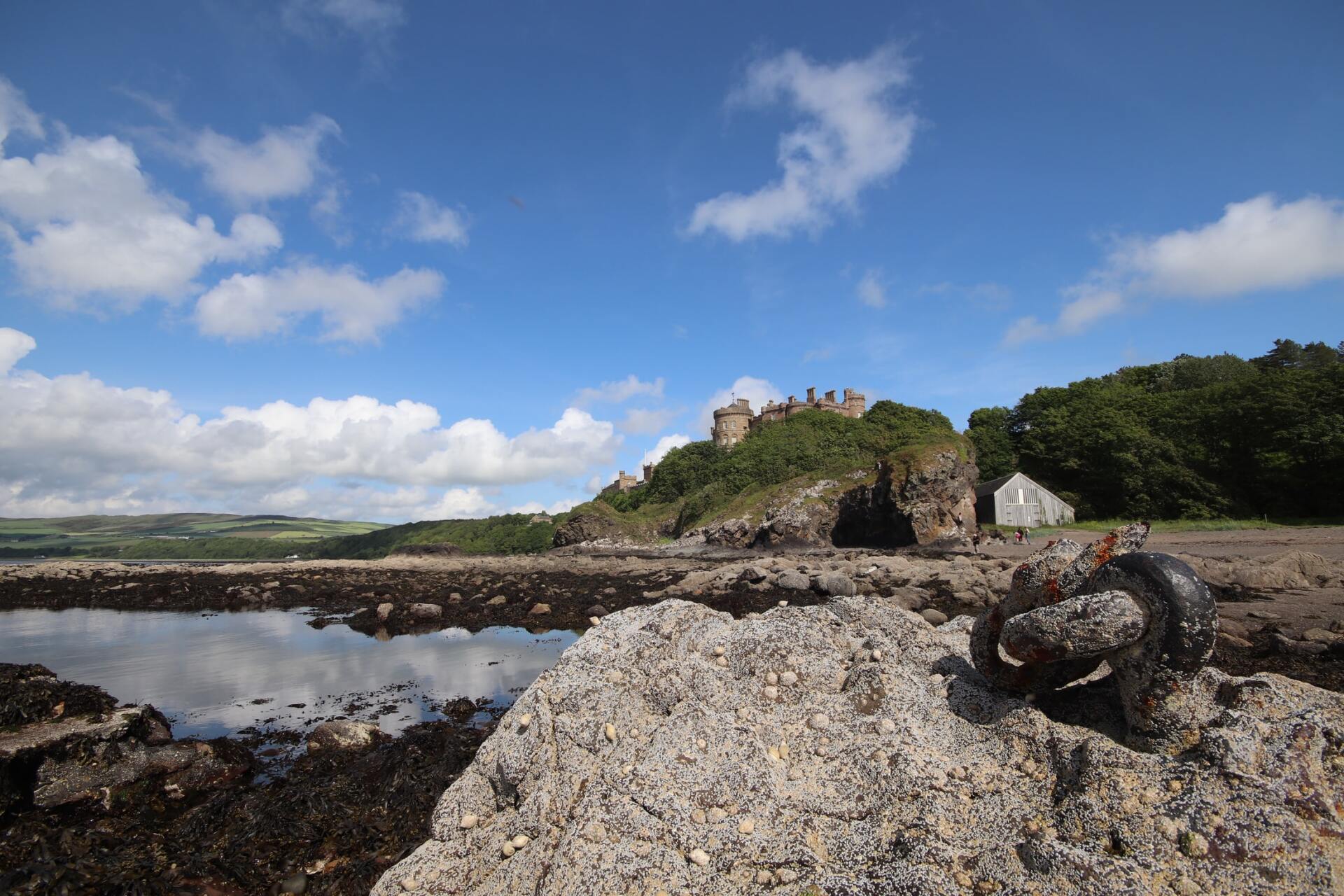 Rocky shoreline with a castle on a hill under a bright blue sky with white clouds.