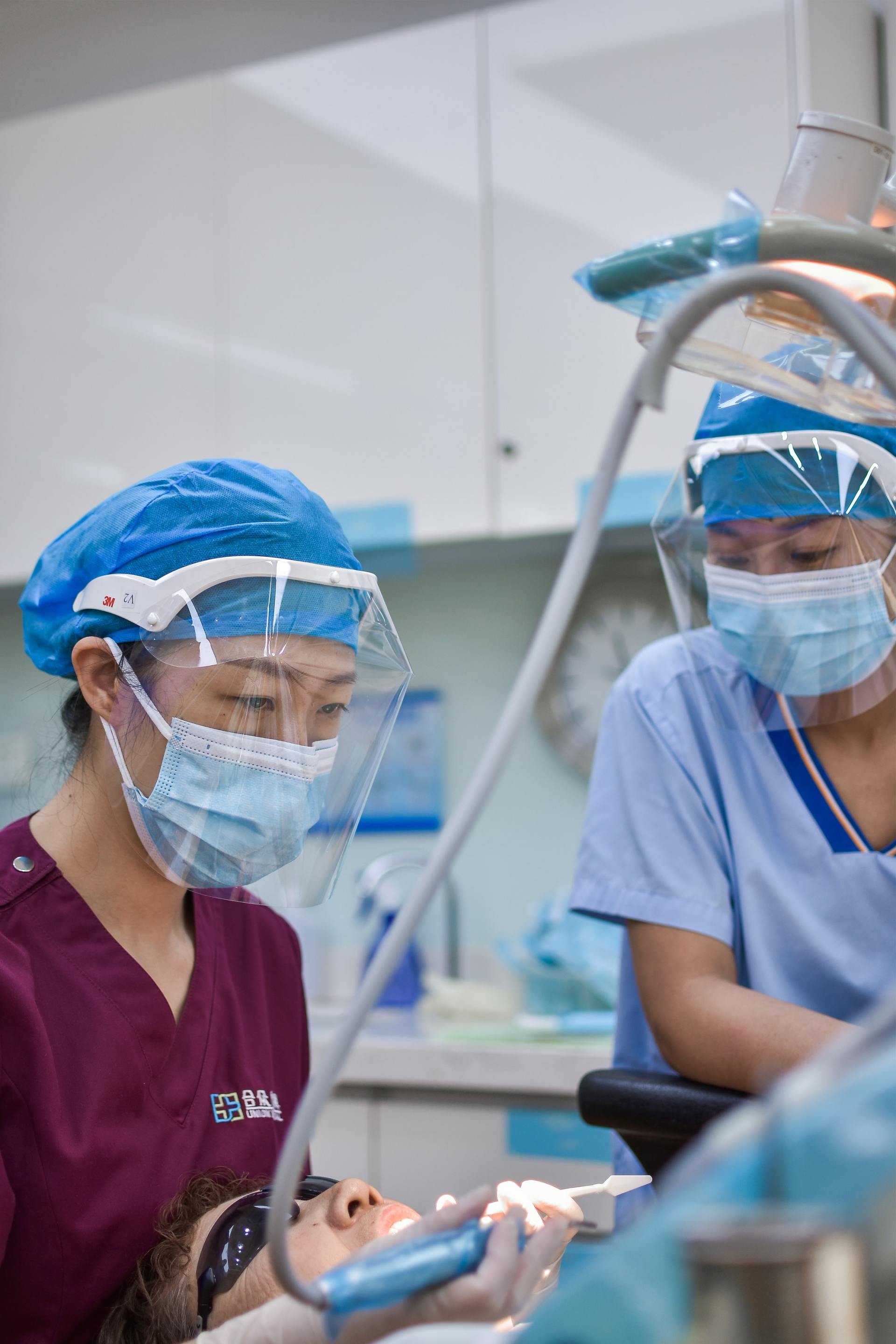 Two dentists in masks and face shields working on a patient in a dental office.