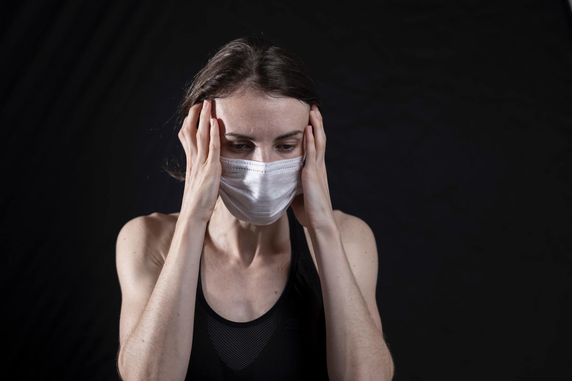 Woman with a mask holding her head