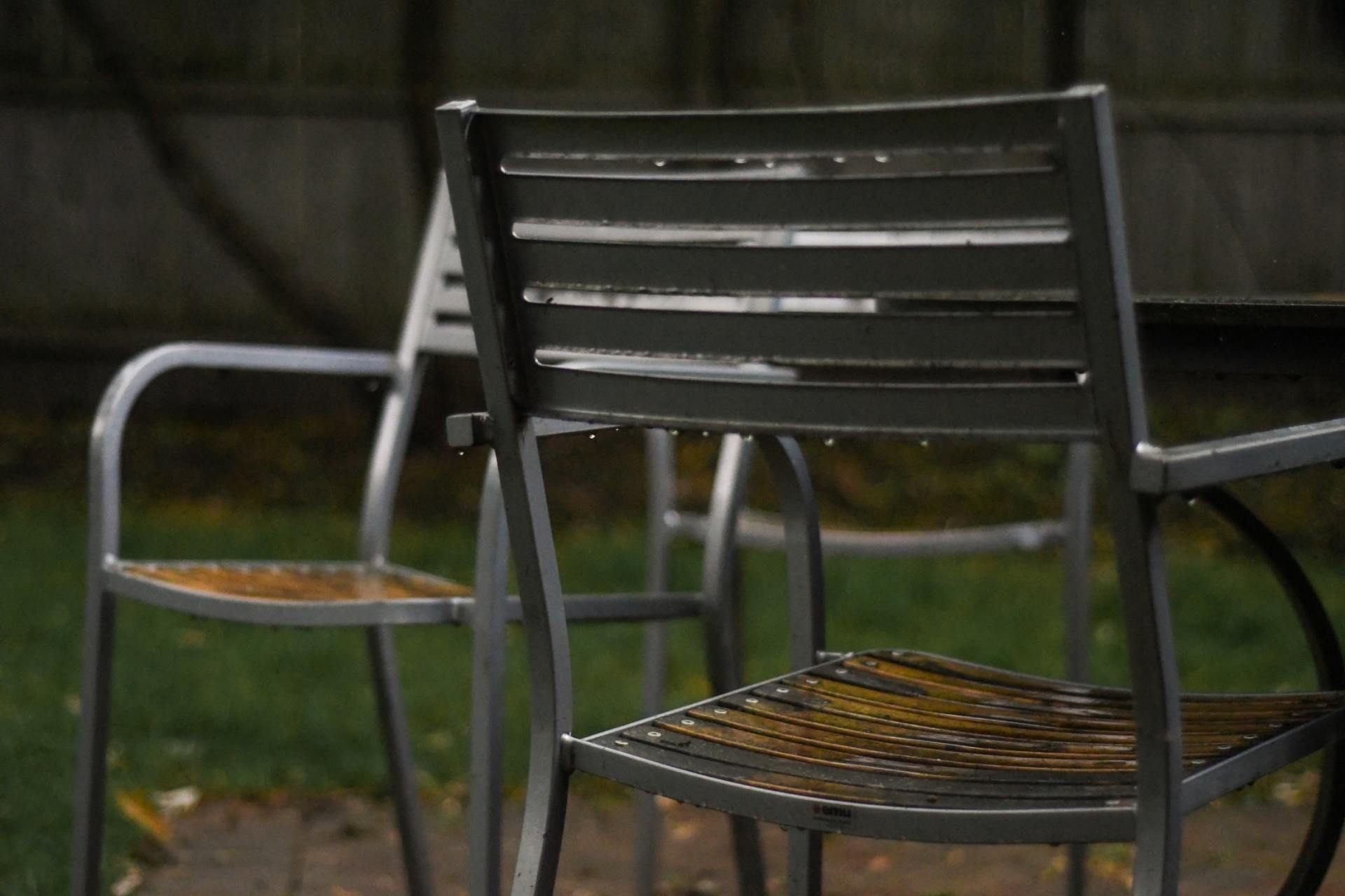 Due sedie da esterno in metallo grigio con gocce di pioggia, posizionate su un patio in un cortile.