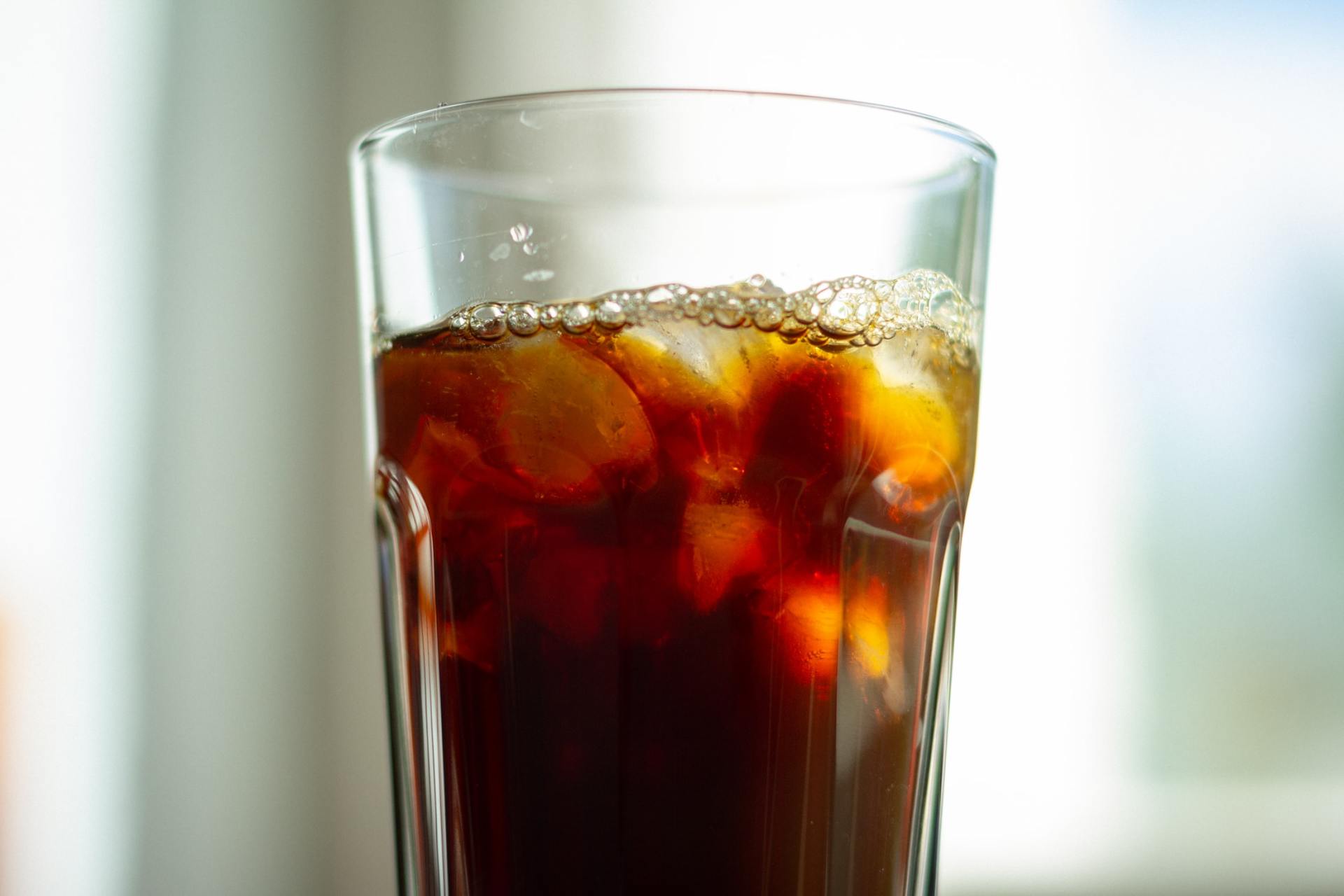 A glass of cola with ice cubes on a table.