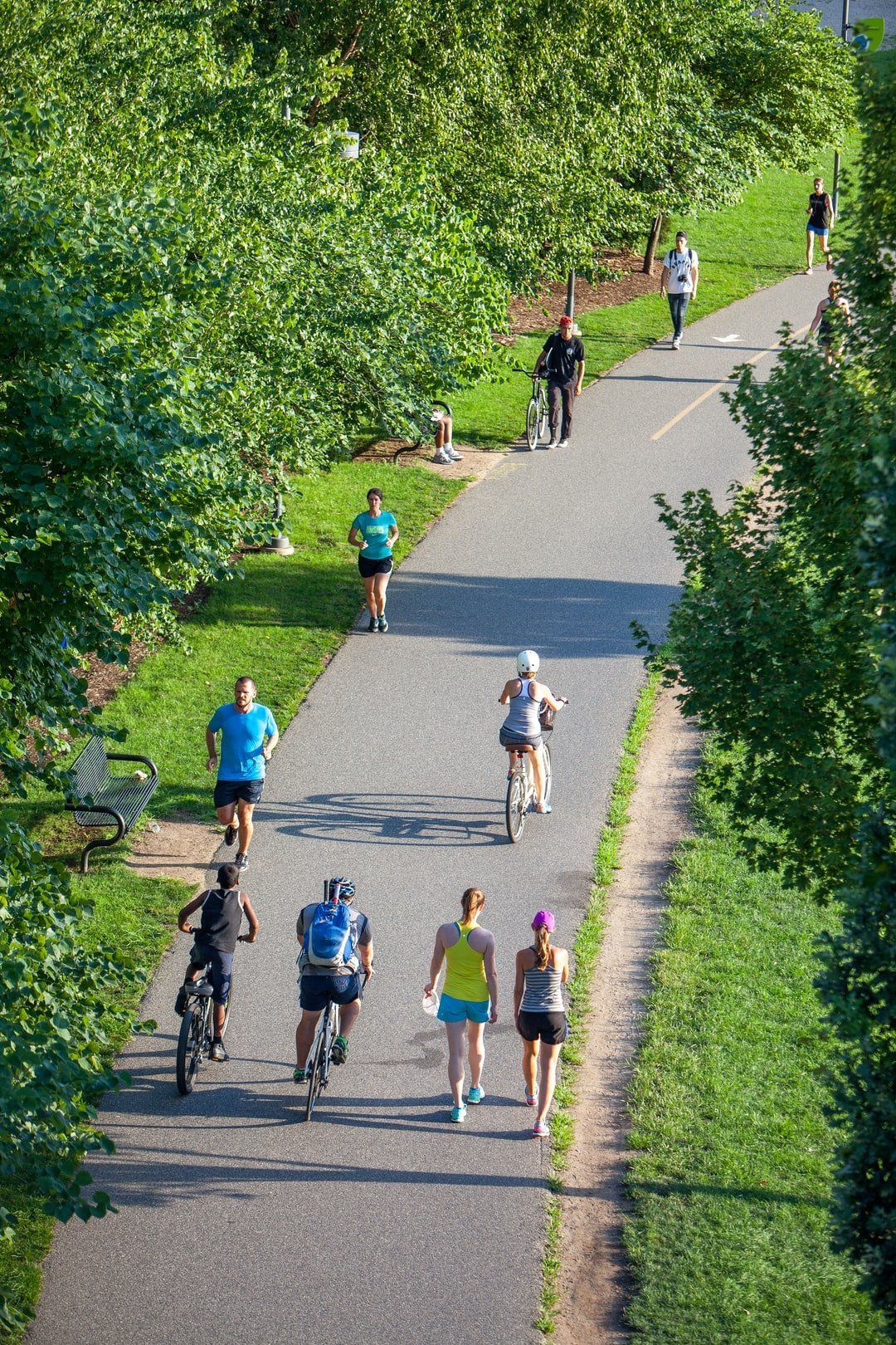 A group of people are walking , riding bikes and running down a path.